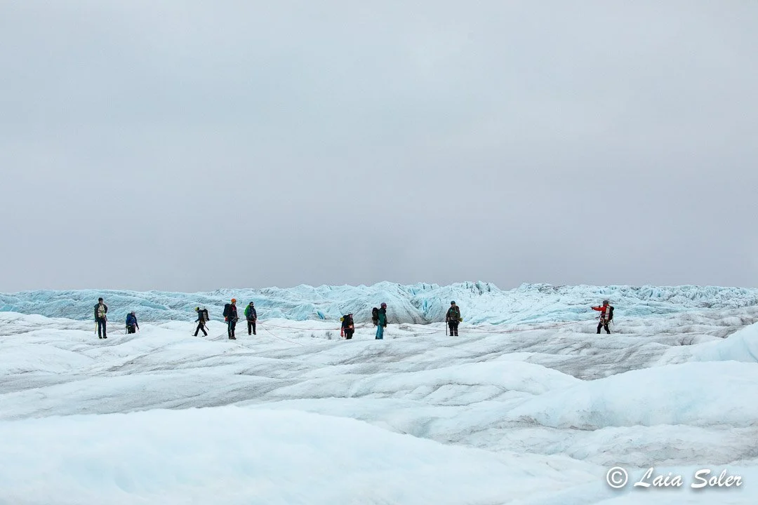 Group of hikers with backpacks walking on a glacier in a cold, icy landscape.