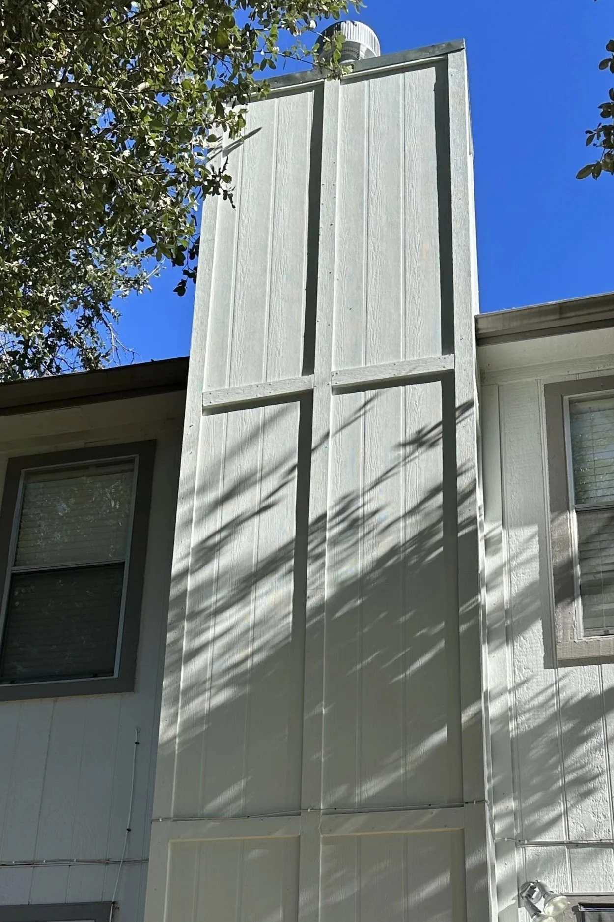 The back of a house with white siding, two windows, and a large vertical wooden panel structure attached to the side. 