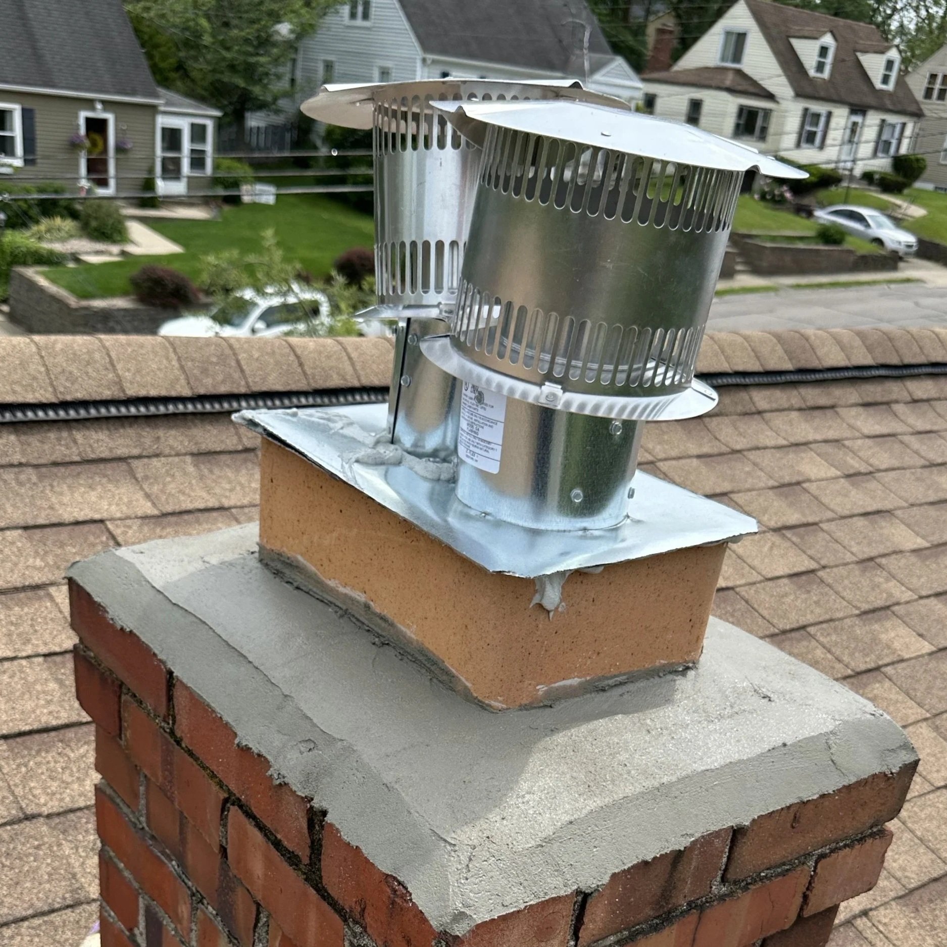 Metal chimney cap installed on a brick chimney on a house roof.
