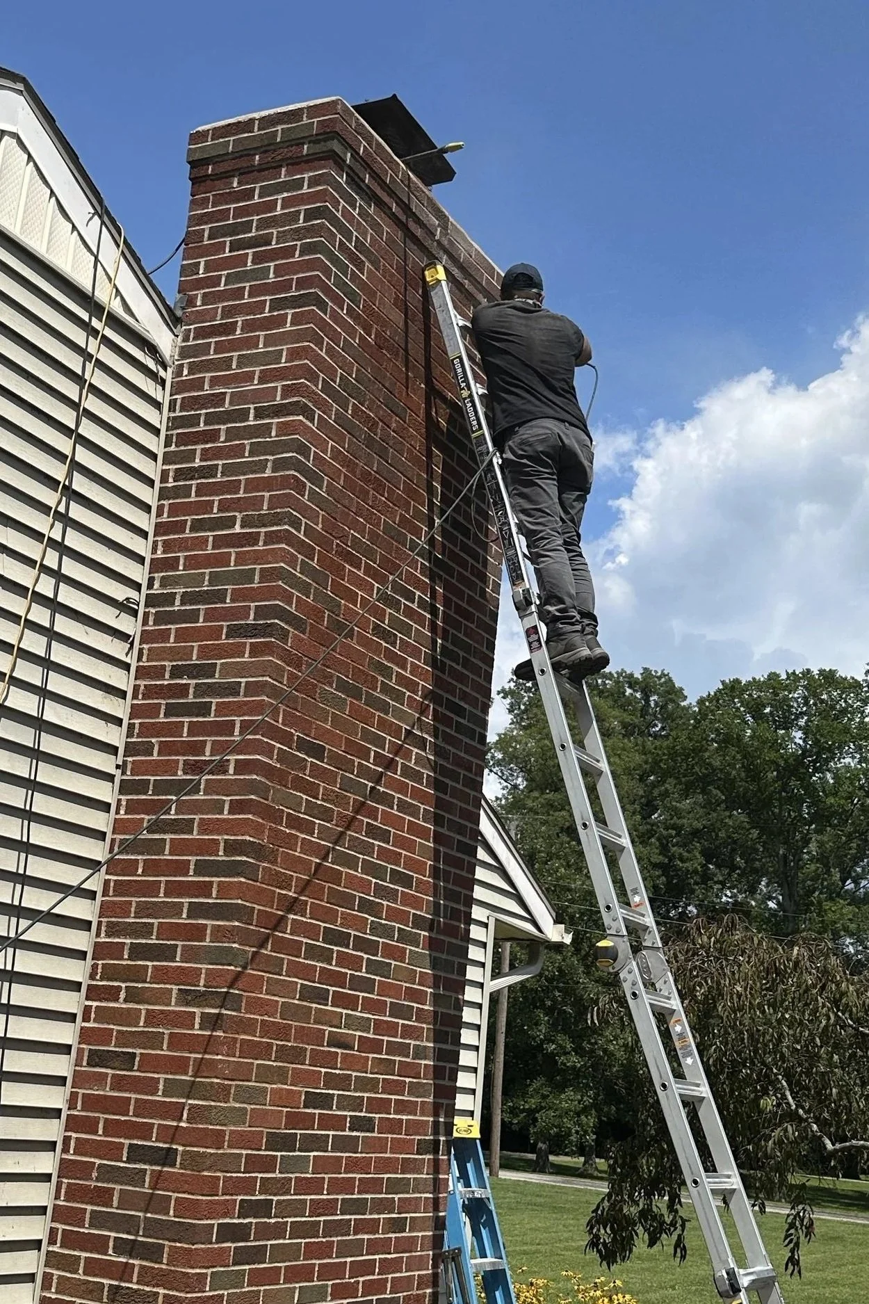 A person climbing an extension ladder against a brick chimney on a house.
