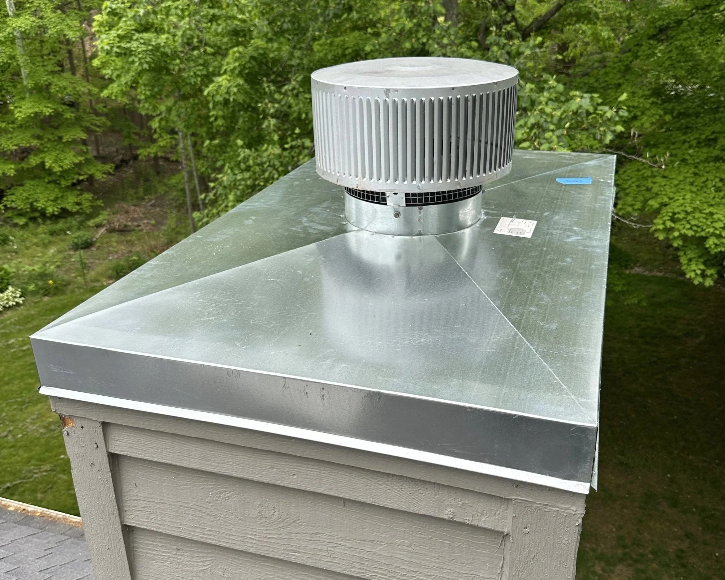 Metal exhaust vent on the roof of a building, with trees in the background.