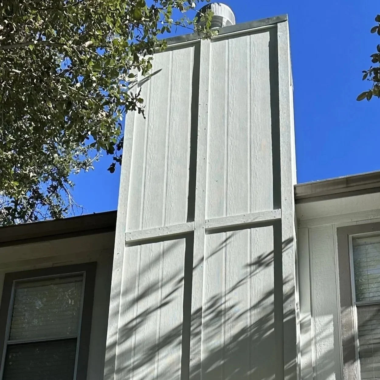 The back of a house with white siding, two windows, and a large vertical wooden panel structure attached to the side. 