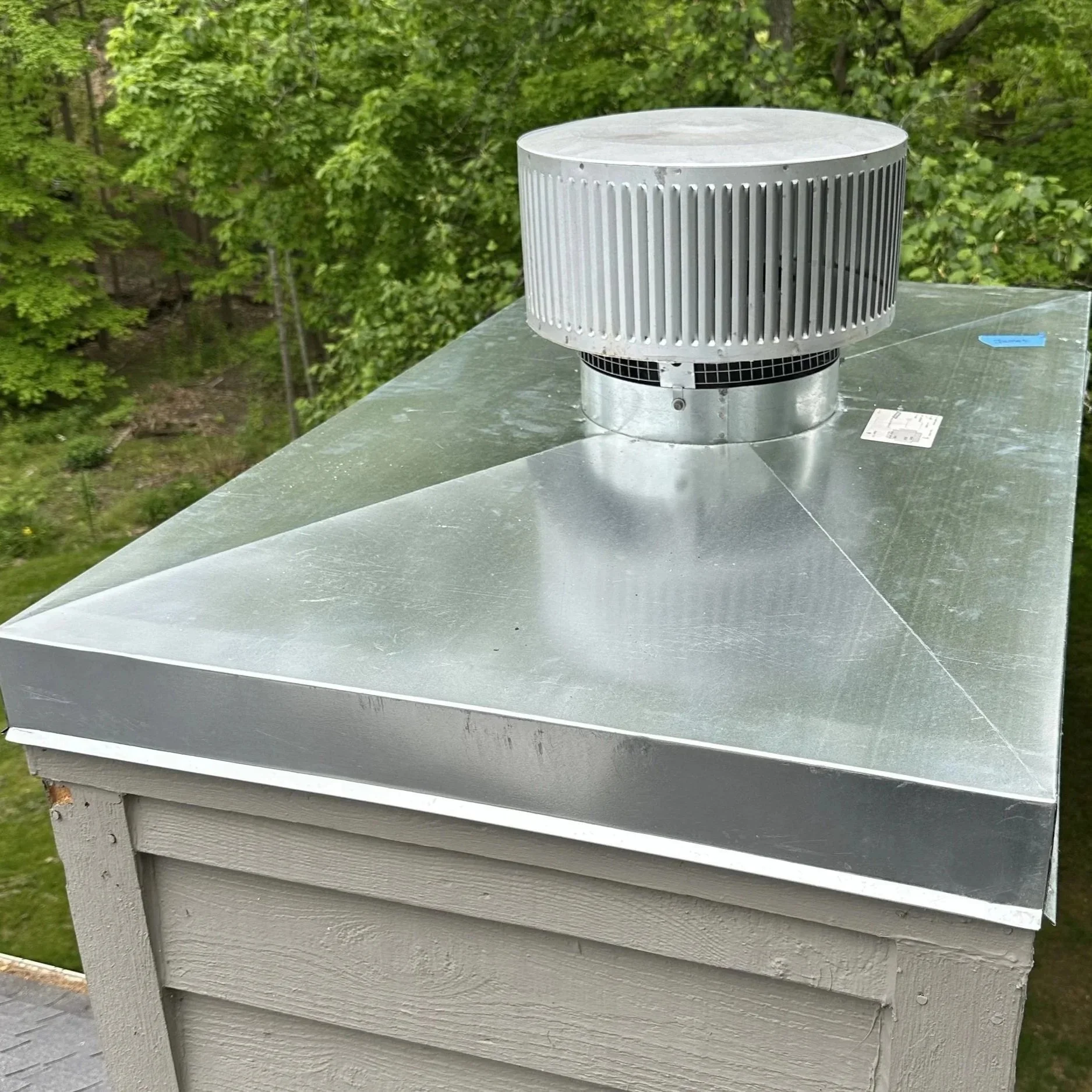 Metal exhaust vent on the roof of a building, with trees in the background.