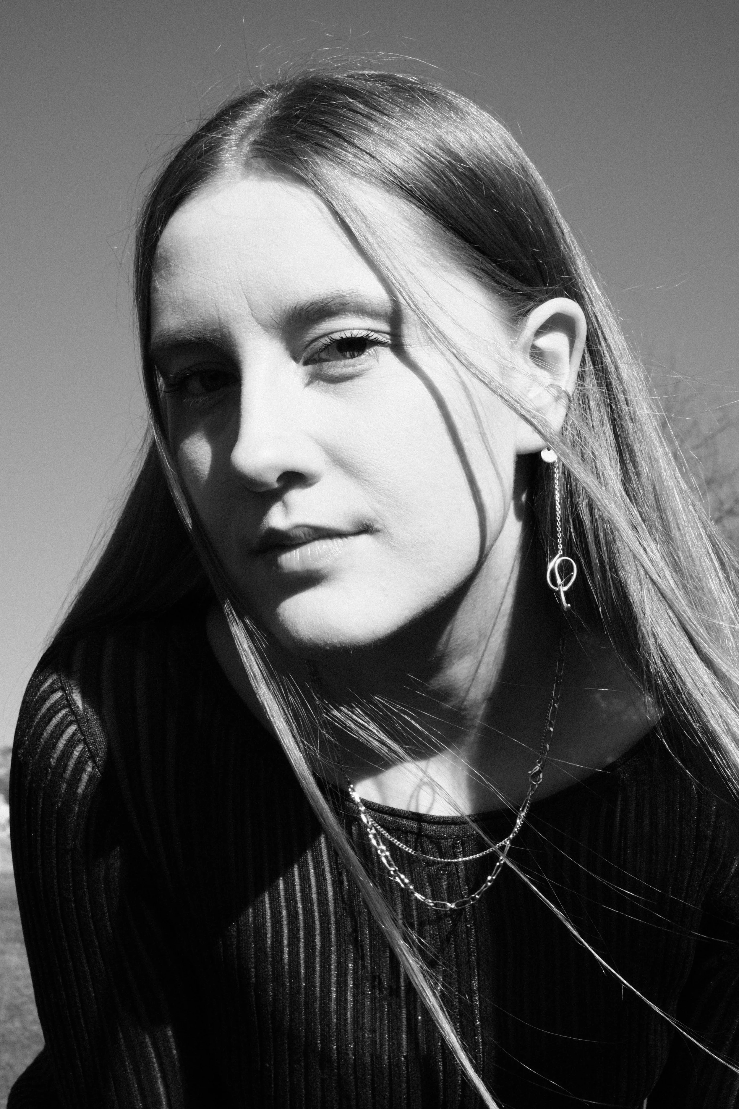 Black and white photo of a woman with long hair, wearing jewelry, looking at the camera with a serious expression.