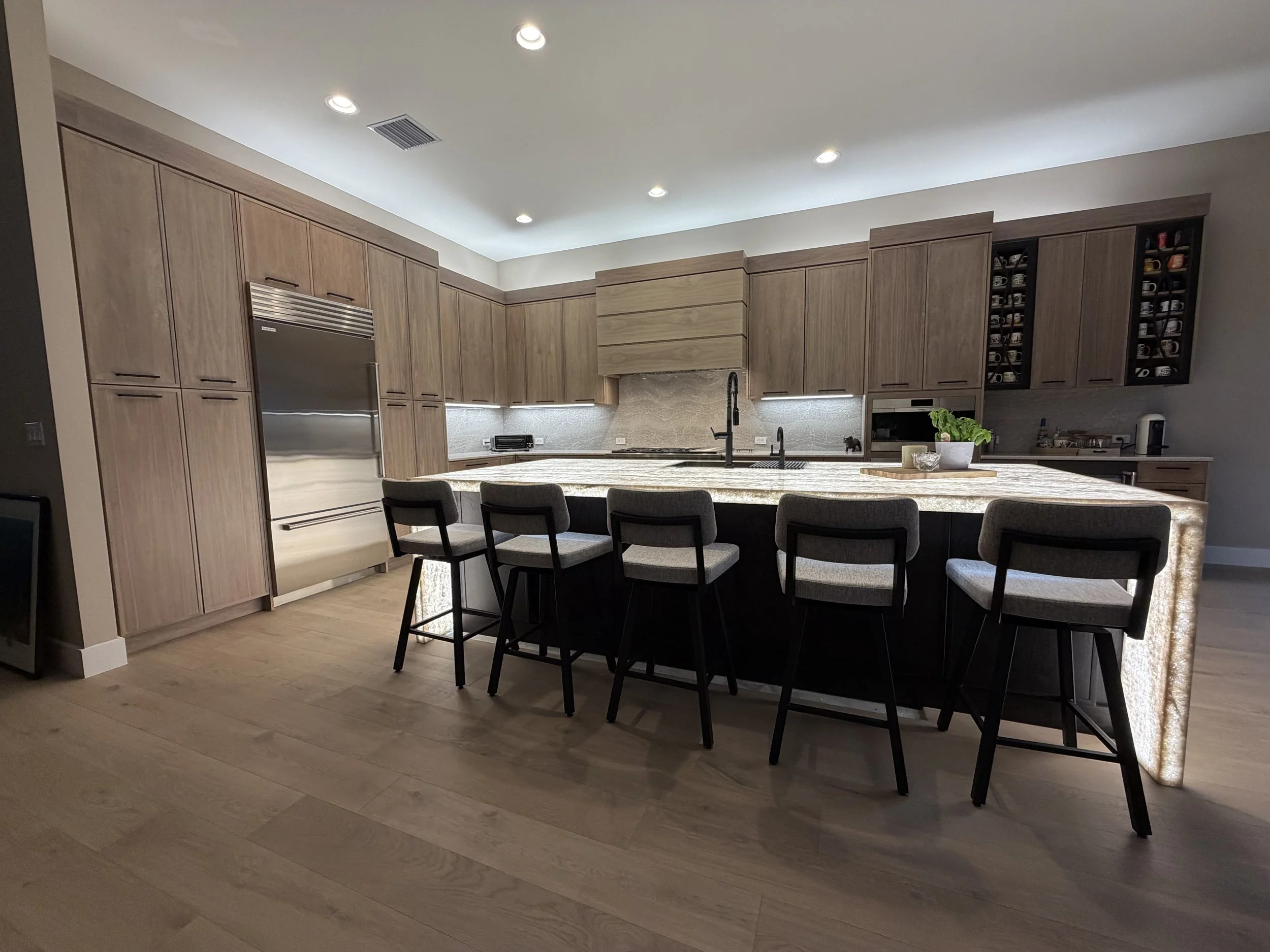 AFTER: Warm wood cabinetry, refined lighting and custom details create a richer, more elevated atmosphere. The redesigned kitchen blends natural materials with contemporary detailing for beautifully integrated high-end aesthetic.