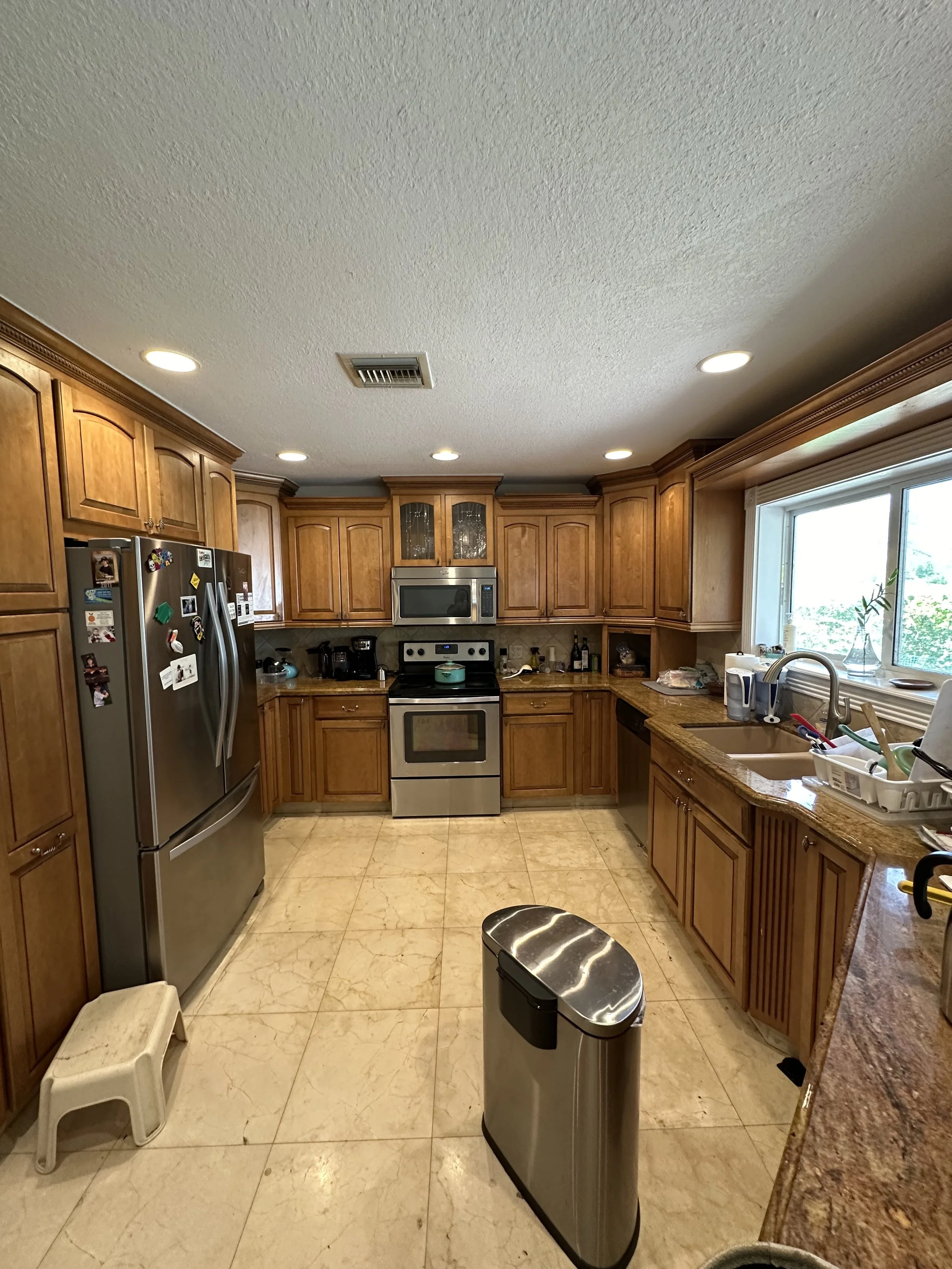 BEFORE: A classic layout burdened by dated wood finishes, bulky overhead cabinetry, and an over-the-range microwave that visually crowded the primary cooking area.