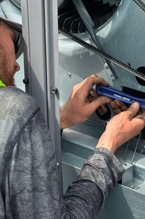 A technician working on a large mechanical or electrical device, using a wrench to tighten a bolt inside a metal casing.