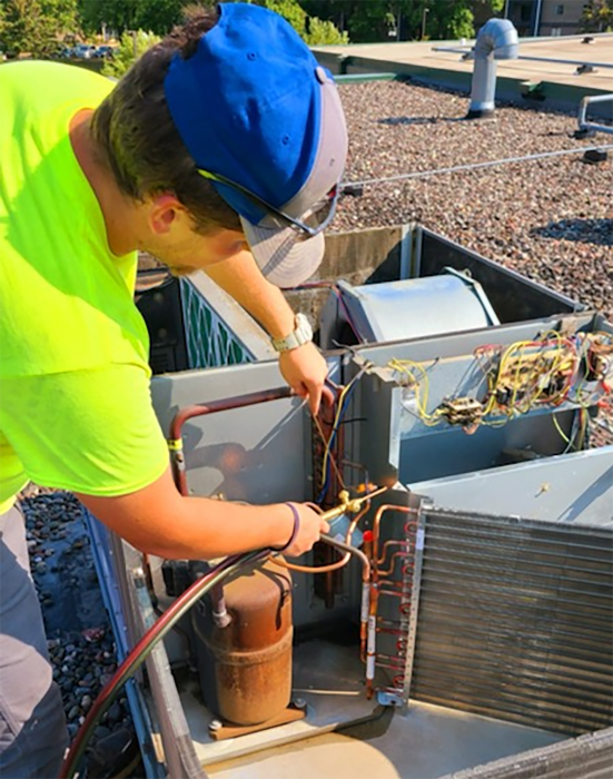 Technician working on HVAC unit on roof, using tools to repair or maintain the system.
