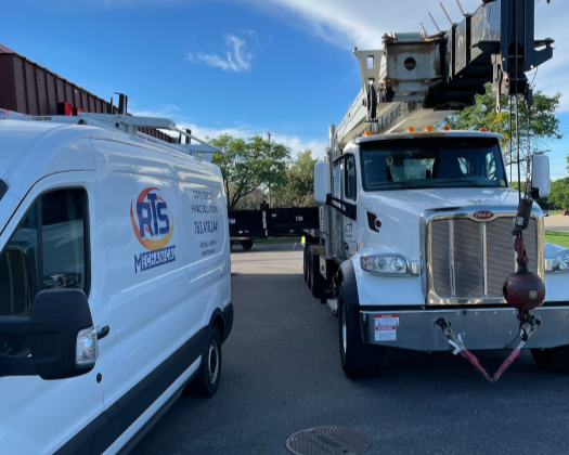 Two work trucks parked outdoors on a sunny day, with a clear blue sky and some trees in the background.