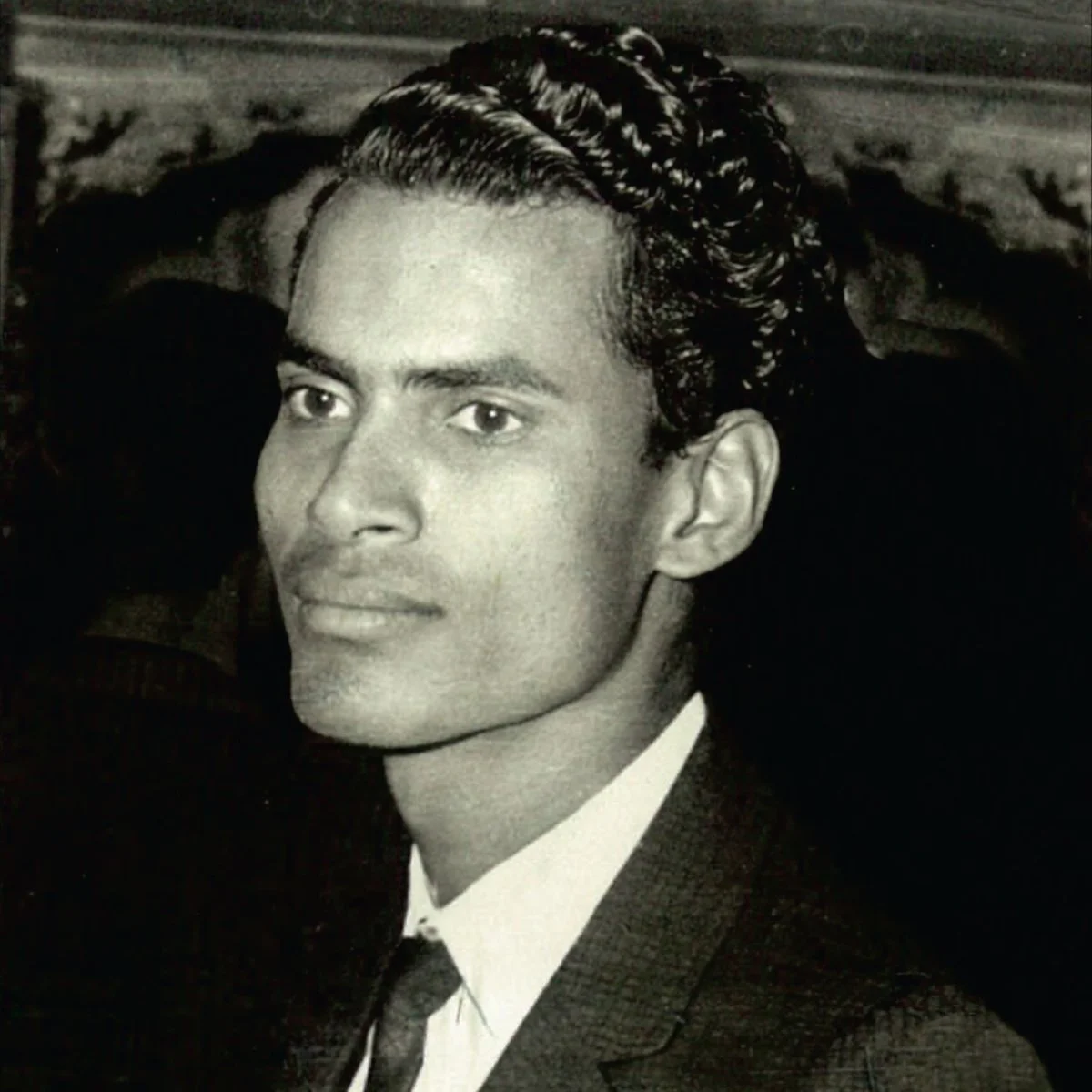 Black and white portrait of a young man with neatly combed hair, wearing a suit and tie, looking slightly to the side.