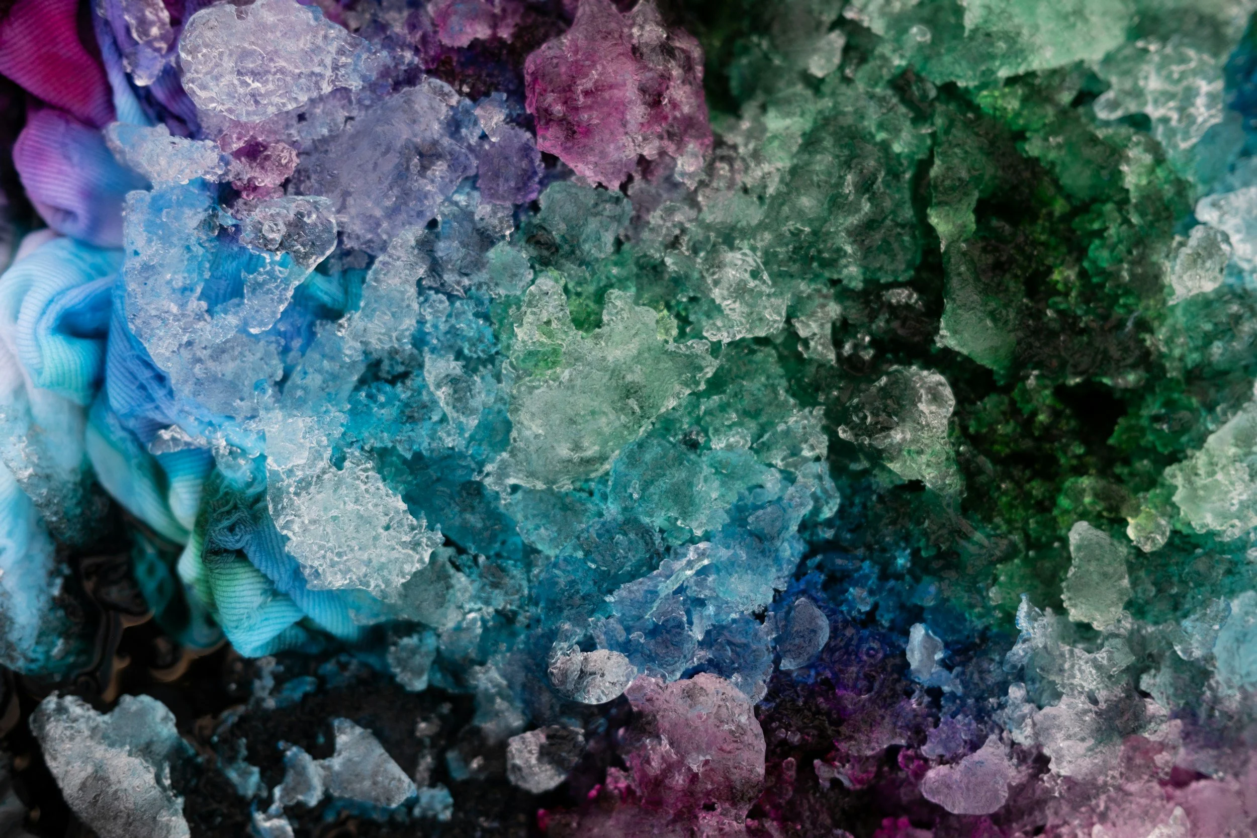 Close-up view of multicolored, fragmented pieces of ice or ice-like crystals in various shades of blue, purple, pink, and green.
