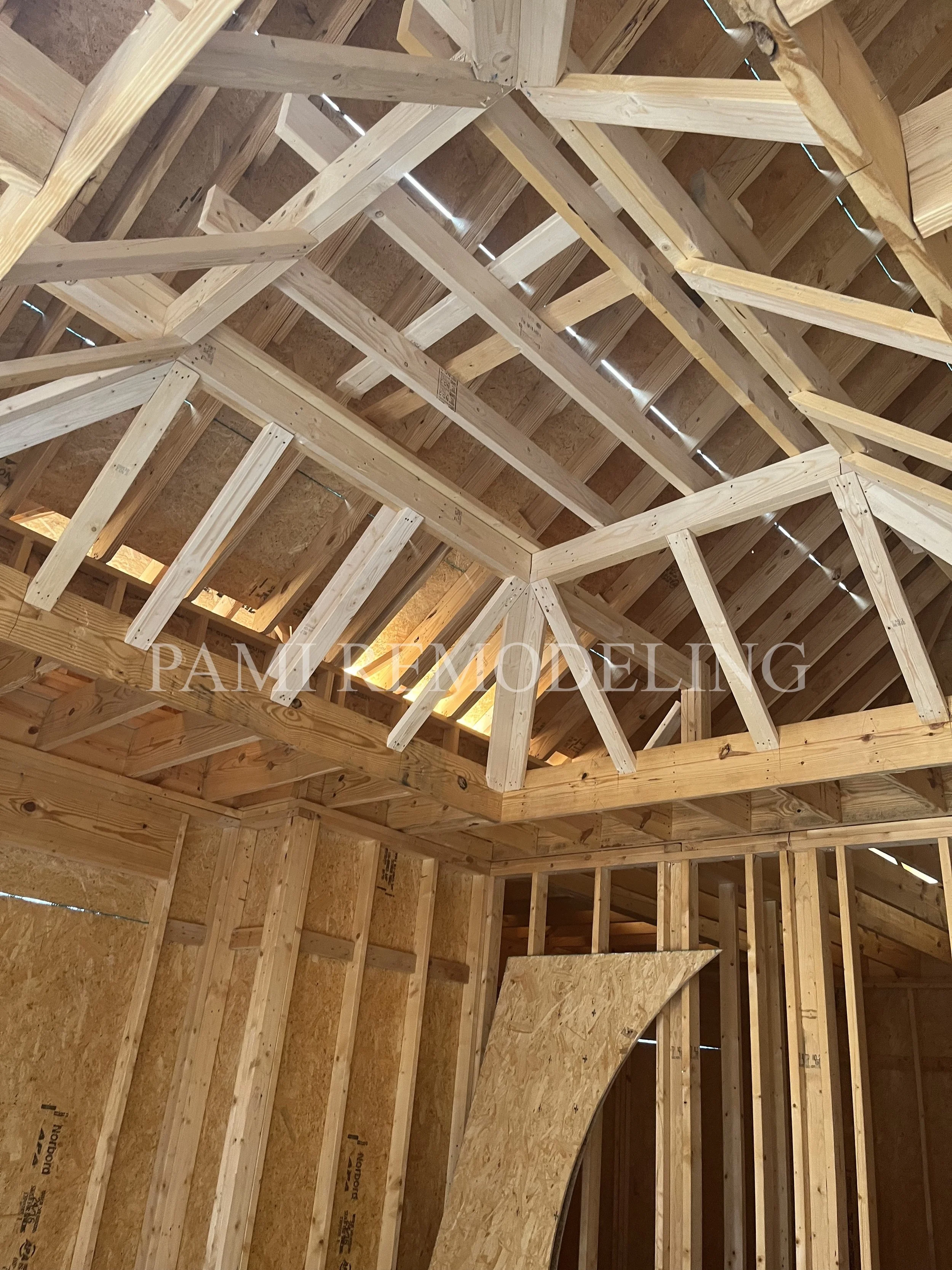 Construction site showing wooden framing for a ceiling and walls, with insulation panels and a curved plywood piece installed.