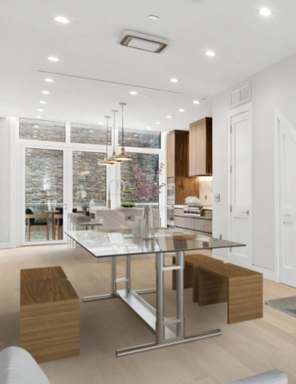 Modern kitchen with wooden cabinets, a marble island, a glass table with metal legs, and two wooden stools, illuminated by pendant and recessed lighting.