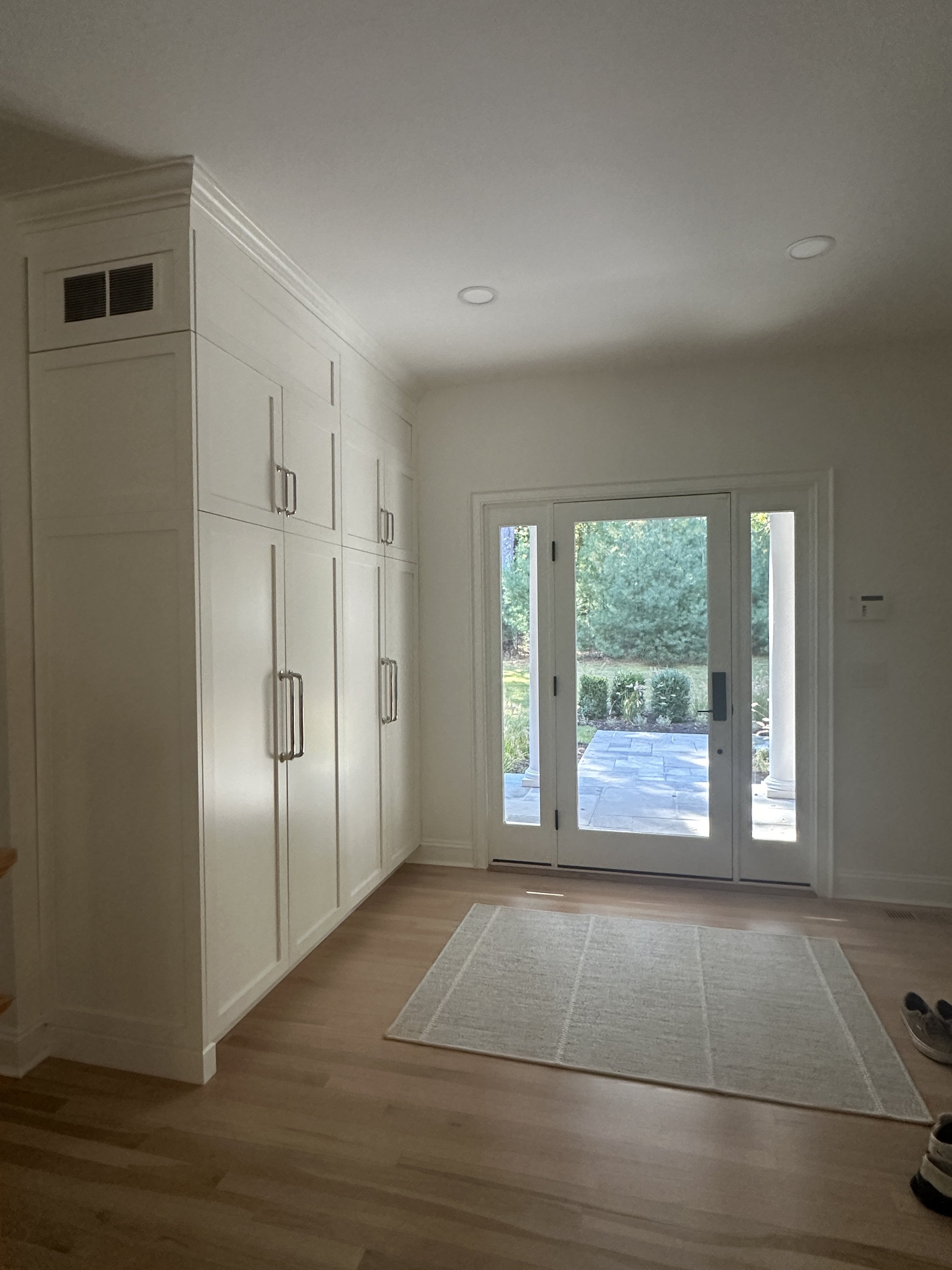 Interior view of a room with white built-in cabinets on the left, a sliding glass door leading to an outdoor patio, and a small beige rug on light hardwood flooring.