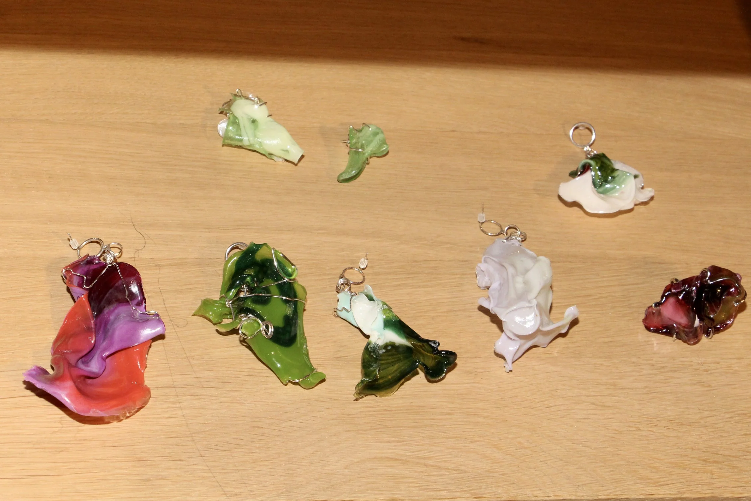 Several colorful glass pendants shaped like flower petals on a wooden surface, each with metal loops for necklaces.
