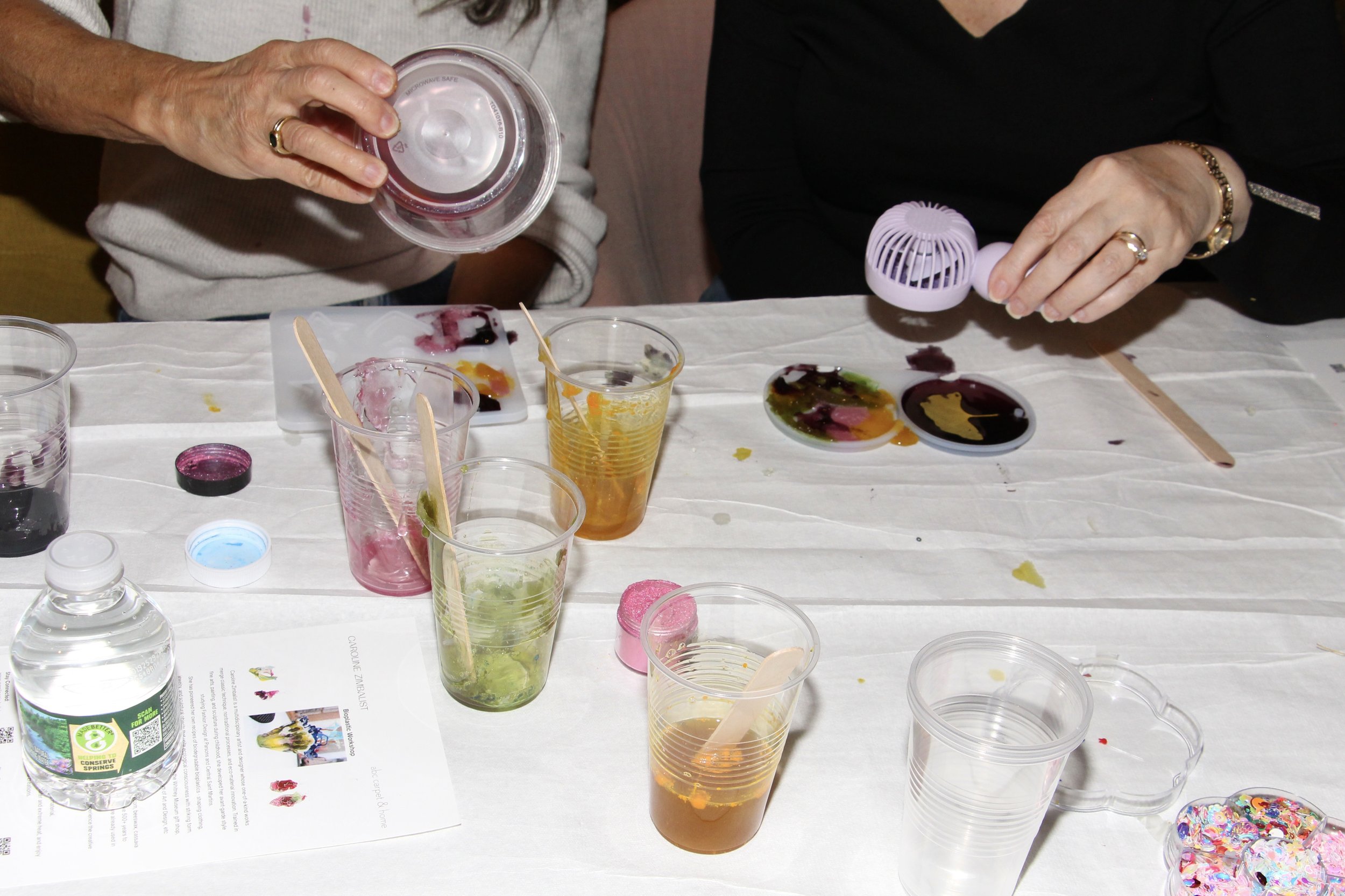 People working on watercolor painting project at a table with paints, brushes, and cups.
