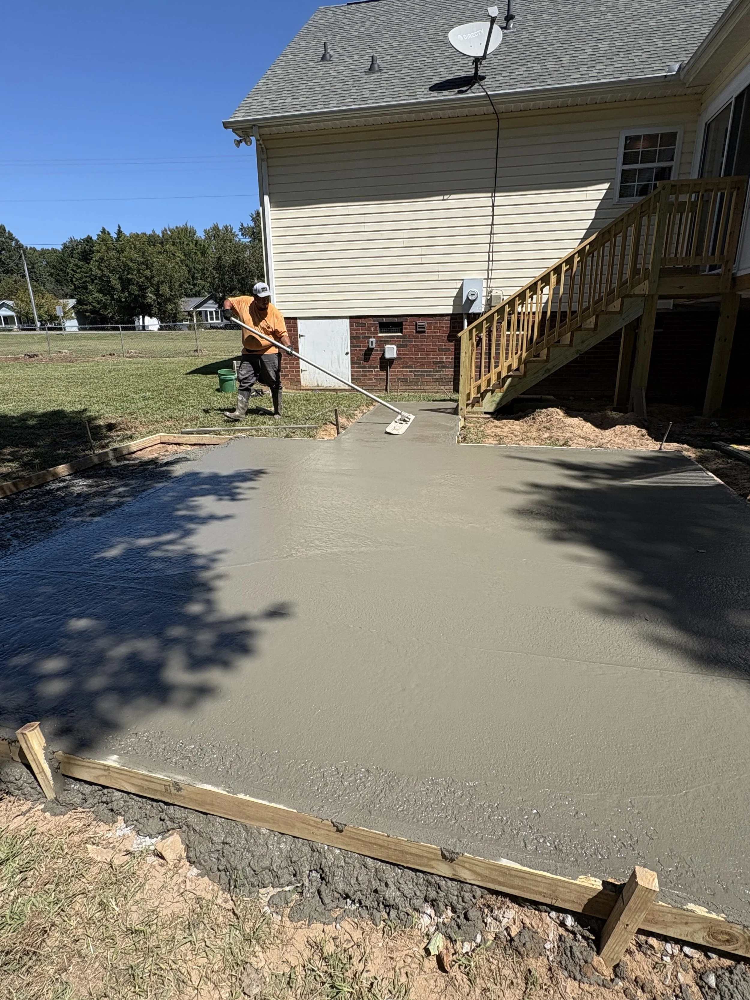 Person pouring wet concrete on a freshly paved area in a backyard.