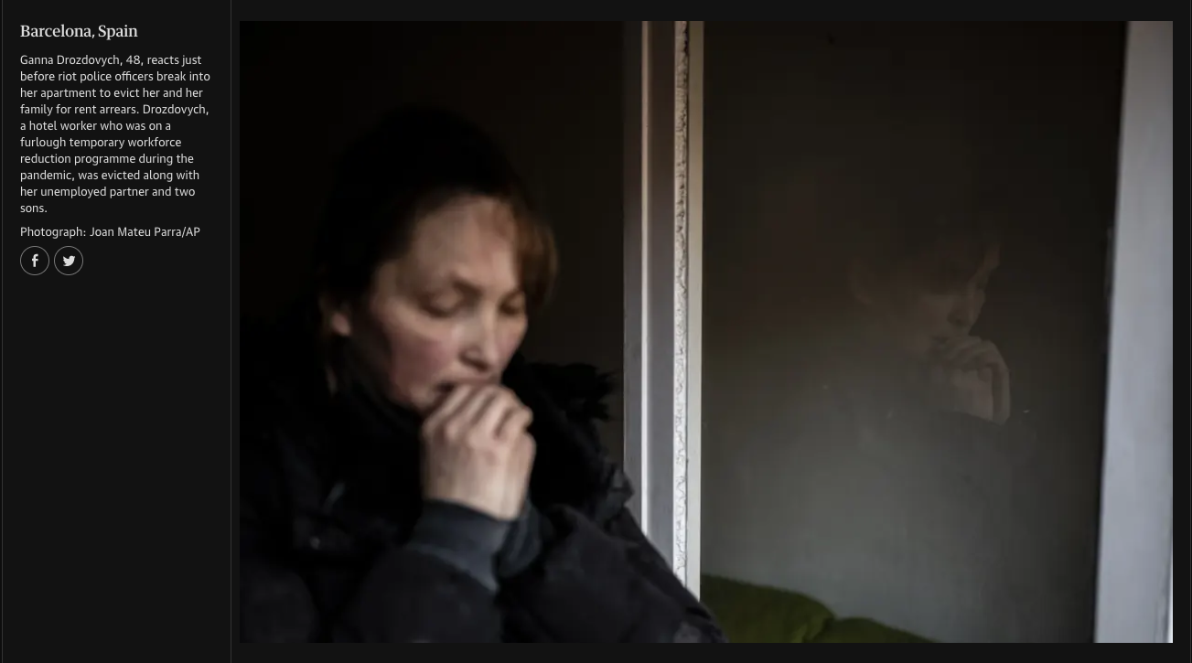 A woman with short brown hair sitting near a window with her hand near her mouth, looking thoughtful or worried. There is a reflection of her on the glass of the window.