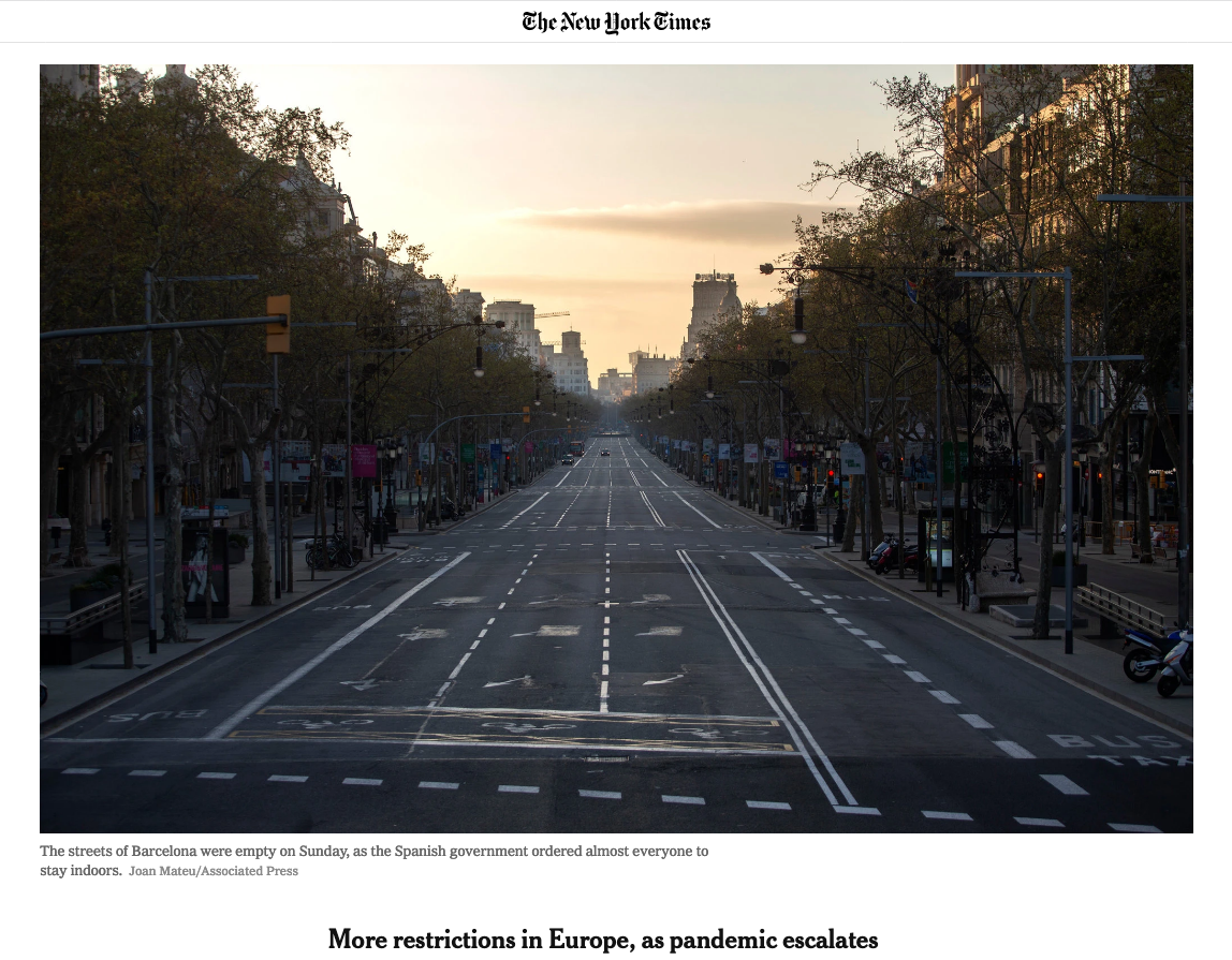 Empty street in Barcelona with marked lanes and trees lining the sidewalks, sunset in the background, and buildings on both sides.