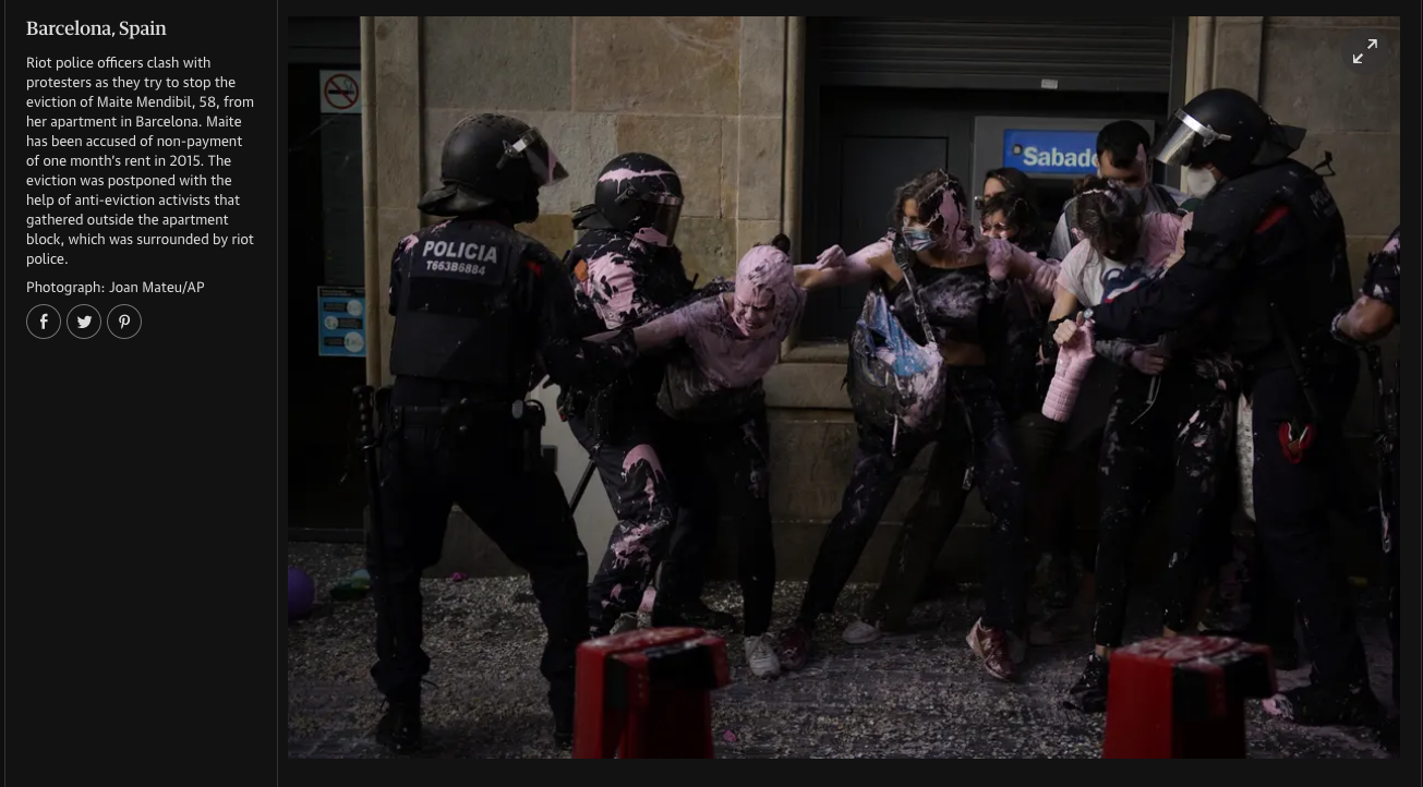 Riot police officers clash with protesters outside a building in Barcelona, Spain, during an eviction attempt of Maite Mendilibar's apartment. The officers are wearing black uniforms and helmets, and some protesters are covered in pink and black pain
