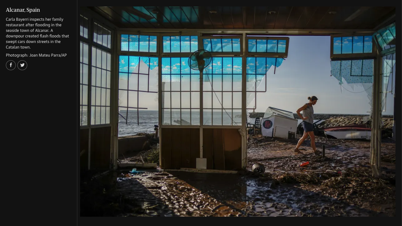 A woman walks through the muddy interior of a seaside building with broken windows, after a flood in Alcanar, Spain. The surrounding area is muddy with boat debris and damaged structures visible outside.