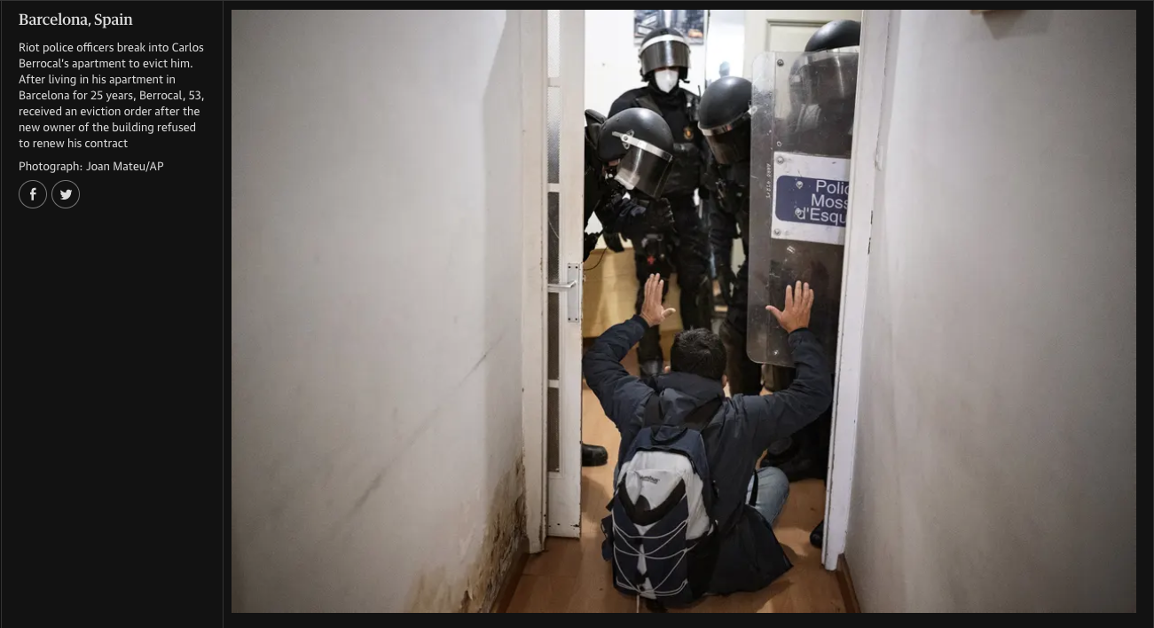 Riot police officers break into Carlos Berrocal's apartment to evict him. A man with a backpack sits on the floor with his hands raised as officers approach through a doorway, with a police shield and helmeted officers visible.