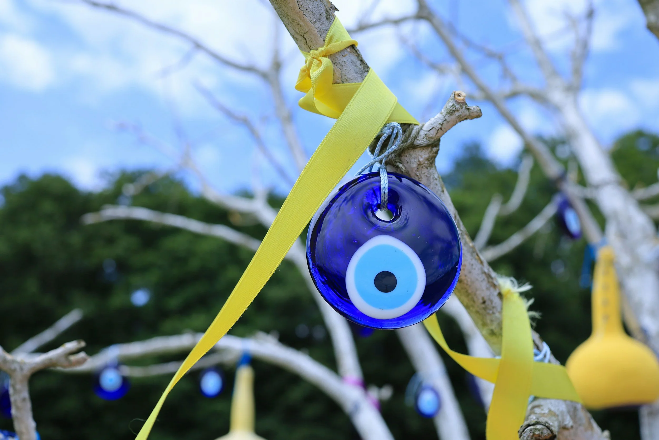 Guiño de ojo de vidrio azul colgado de un árbol con cintas amarillas