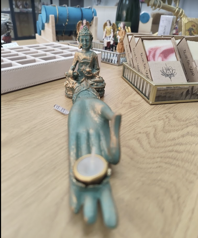 Figuras decorativas, incluyendo una figura de Buda y una mano que sostiene una vela, en una mesa exhibidora.