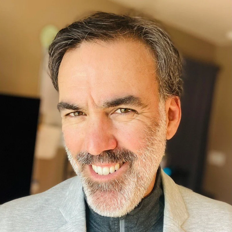 A close-up of a middle-aged man with gray hair and beard, smiling and looking at the camera.