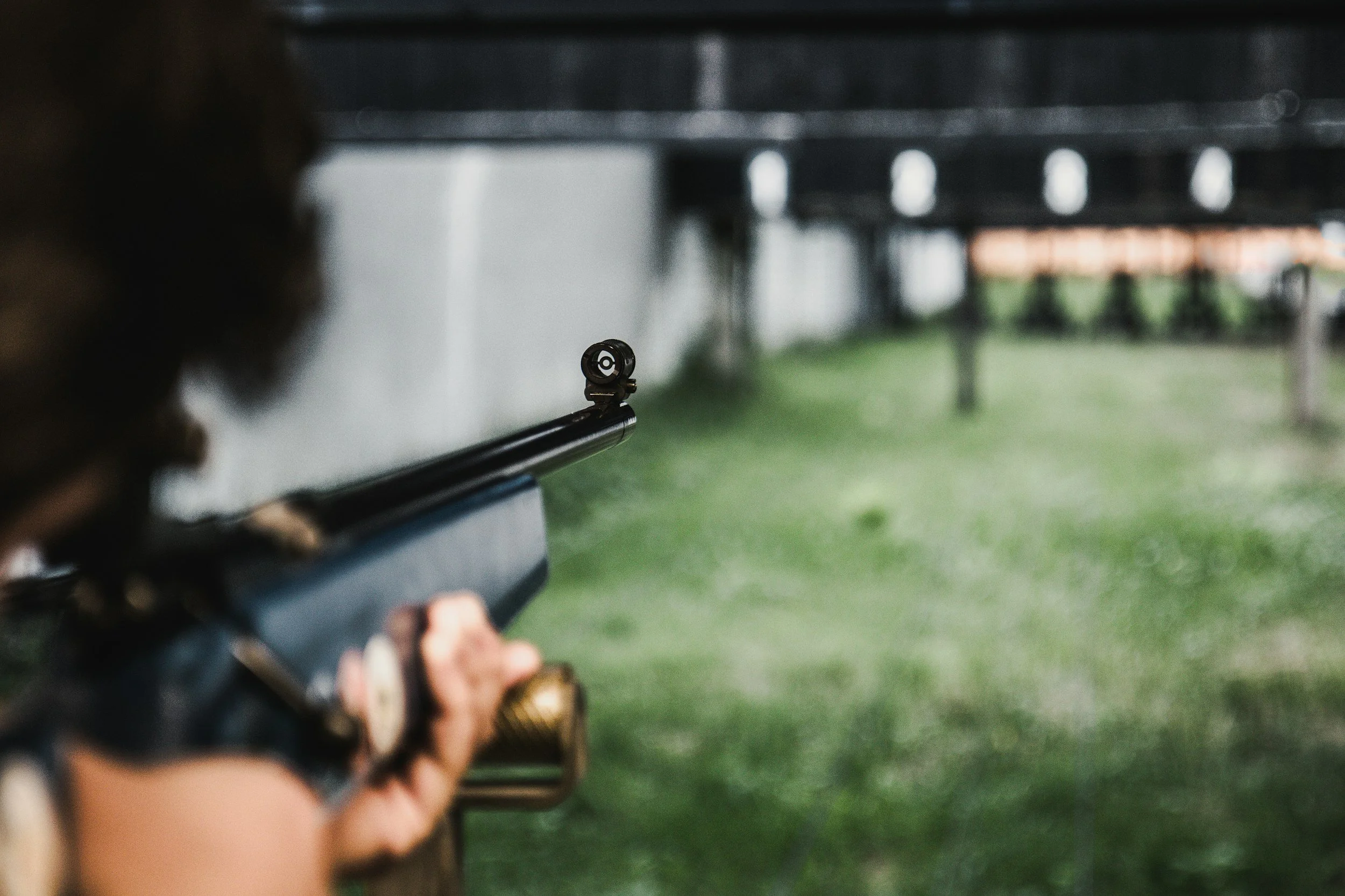 A person aiming a rifle at a shooting range, with the sights aligned towards targets in the distance.