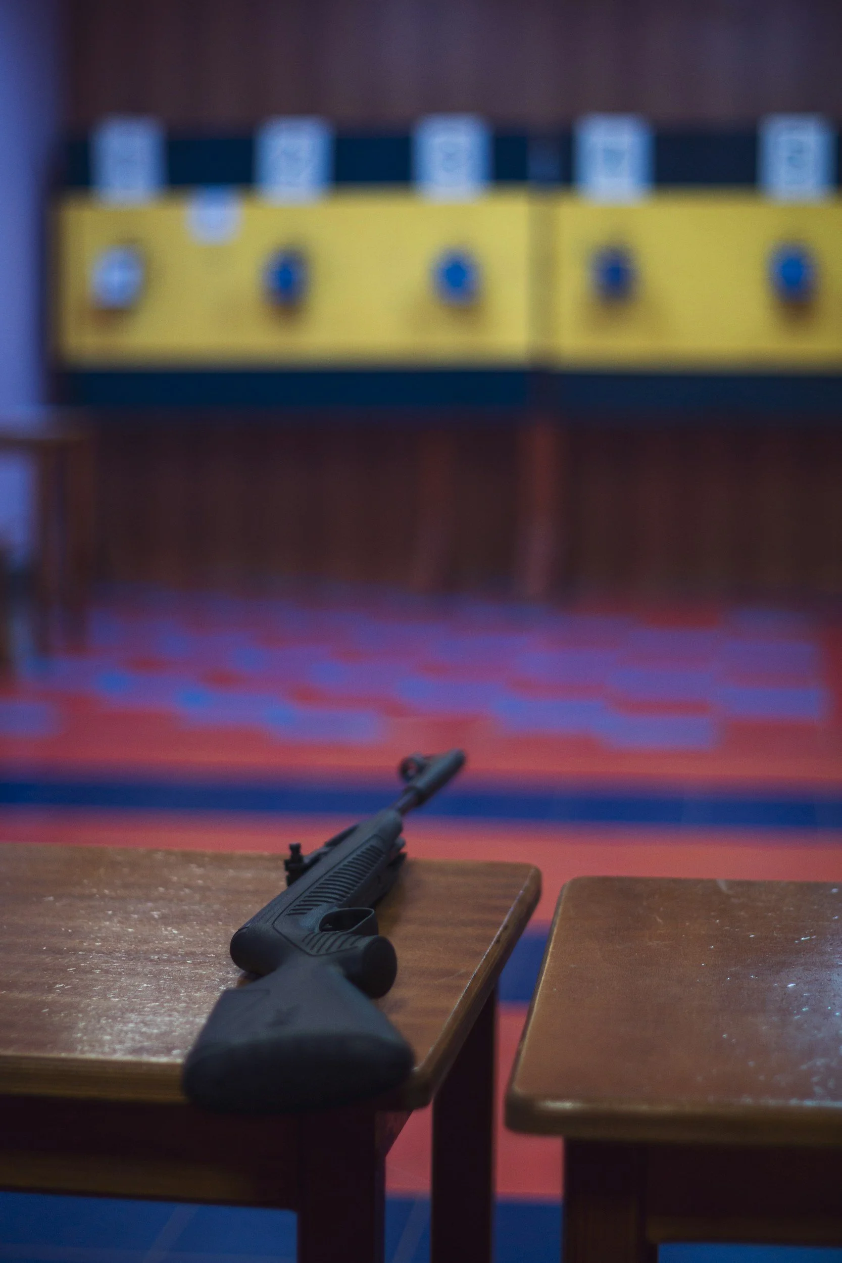 A handgun resting on a wooden table in an indoor shooting range, with colorful bullet targets on the wall in the background.