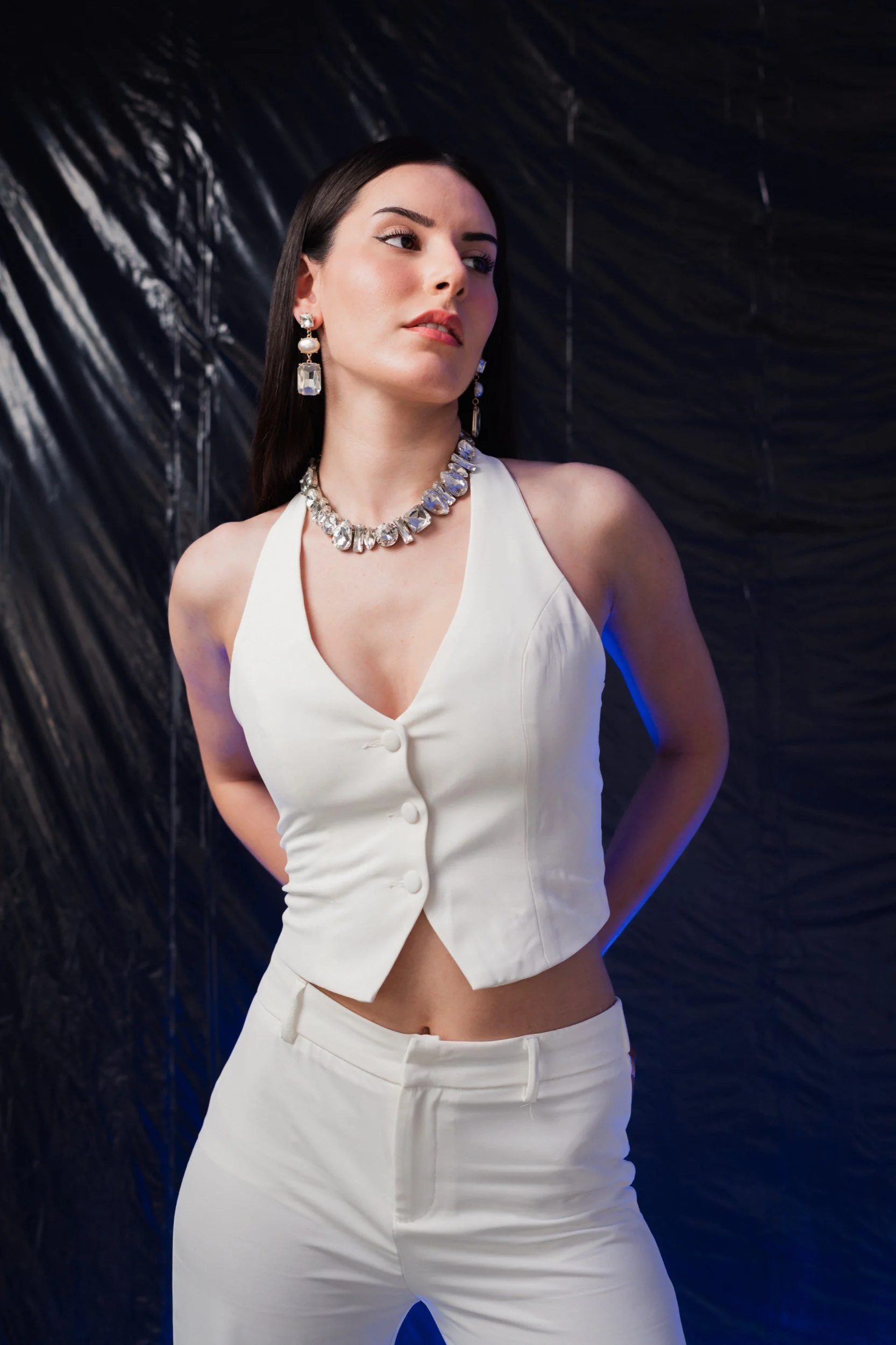 Frau in weißem Outfit mit Schmuck vor dunklem Hintergrund