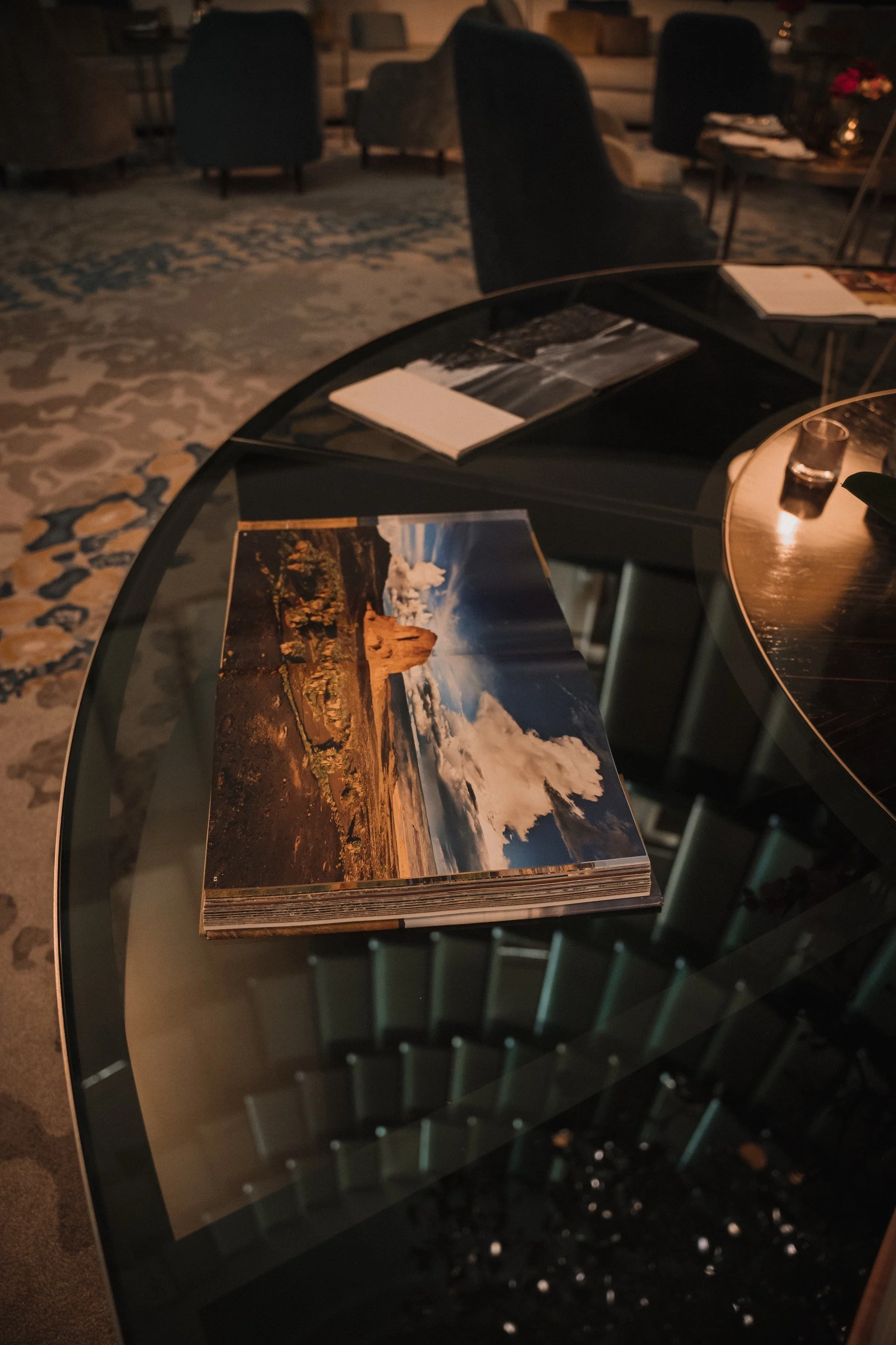 Fotobuch mit einem Bild einer Wüstenlandschaft mit Steinformation, Himmel und Wolken, auf einer dunklen Glas-Tischplatte in einem eleganten Raum.