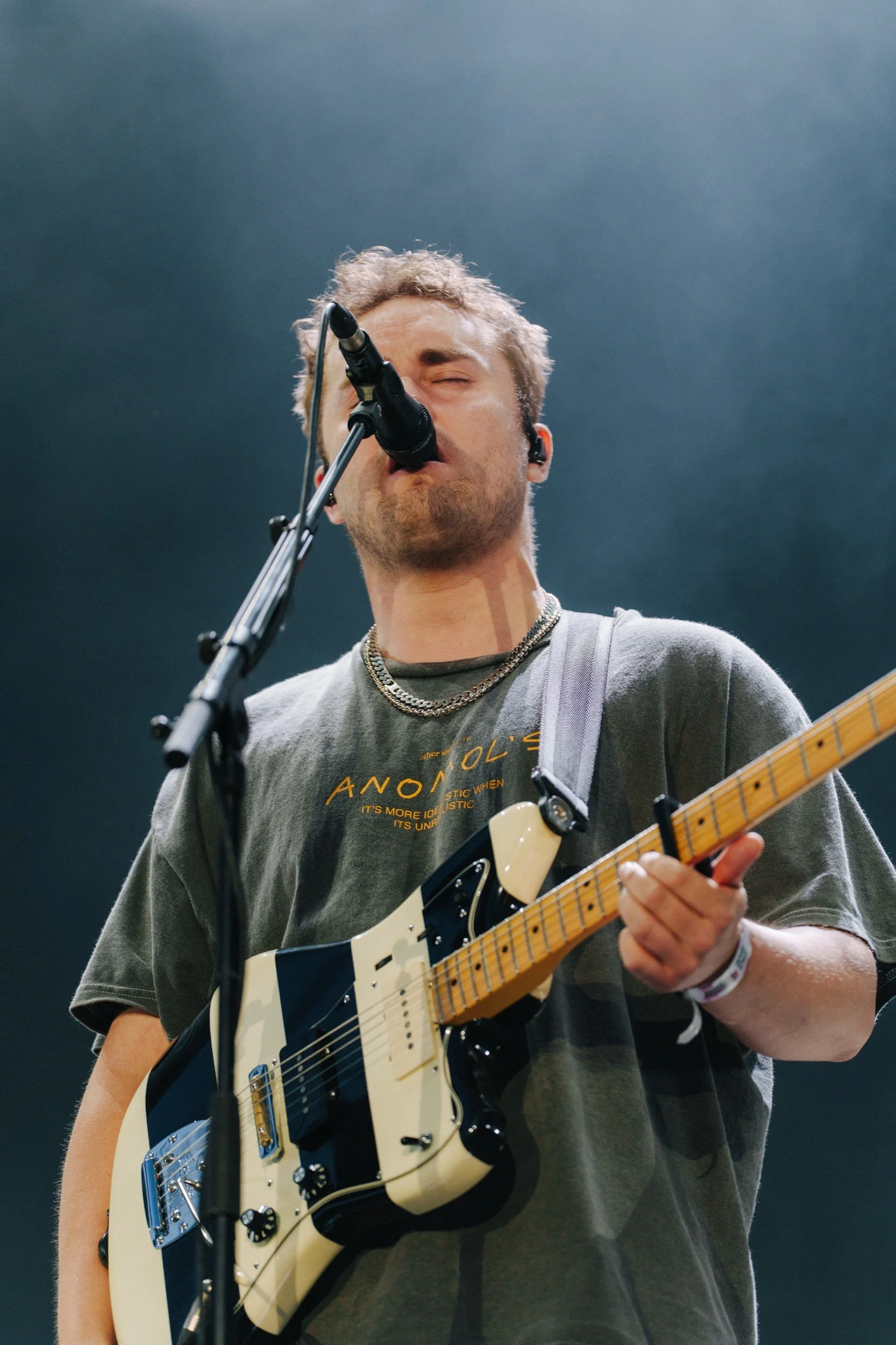 Ein junger Mann singt in einem Mikrofon und spielt Gitarre bei einem Live-Konzert, blickt mit geschlossenen Augen.