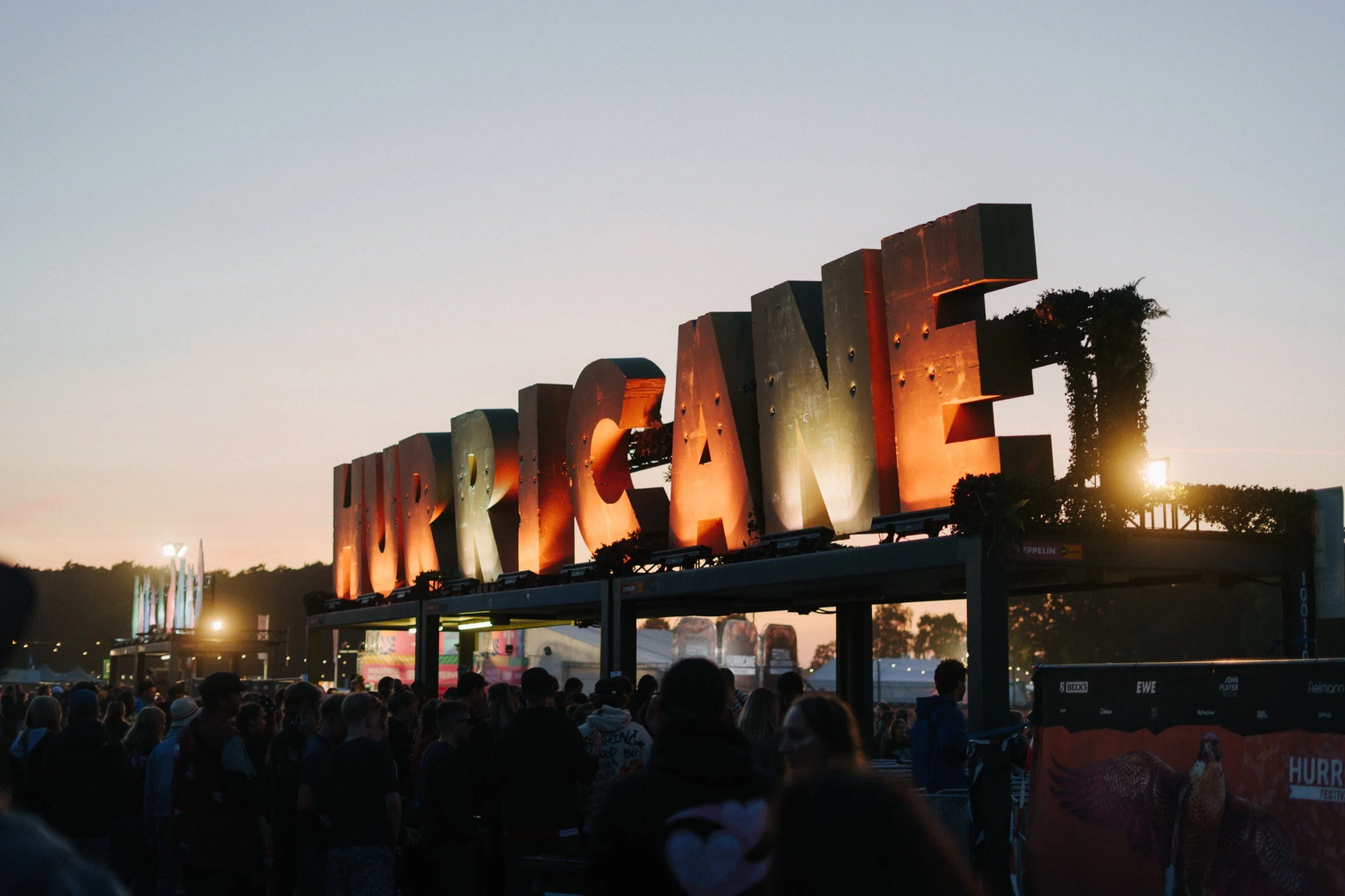 HURRICANE Schriftzug auf einem Festival bei Sonnenuntergang, voll mit Menschen im Vordergrund.