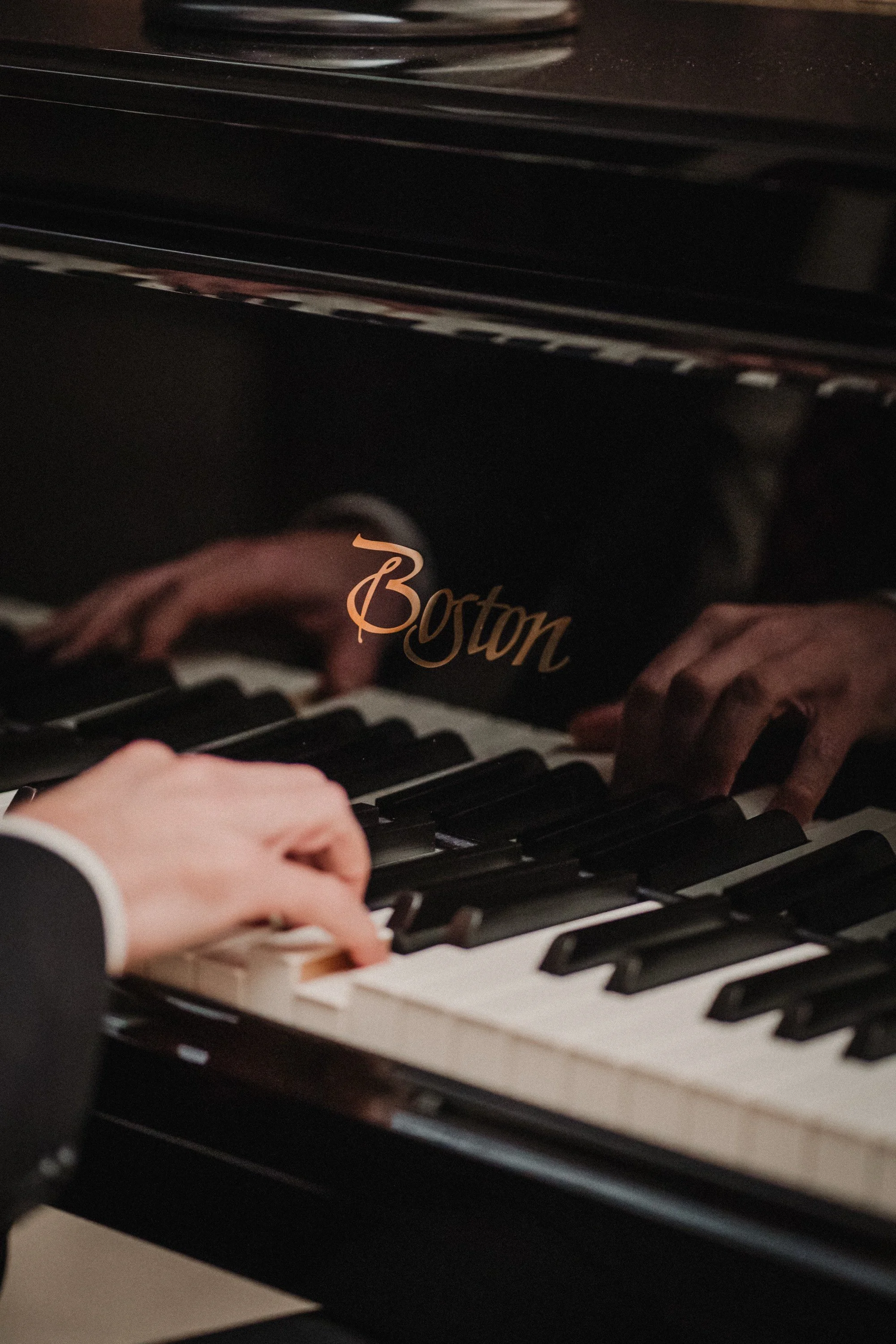 Nahaufnahme von Händen, die auf einer schwarzen und weißen Klaviatur eines Boston-Flügel spielen.