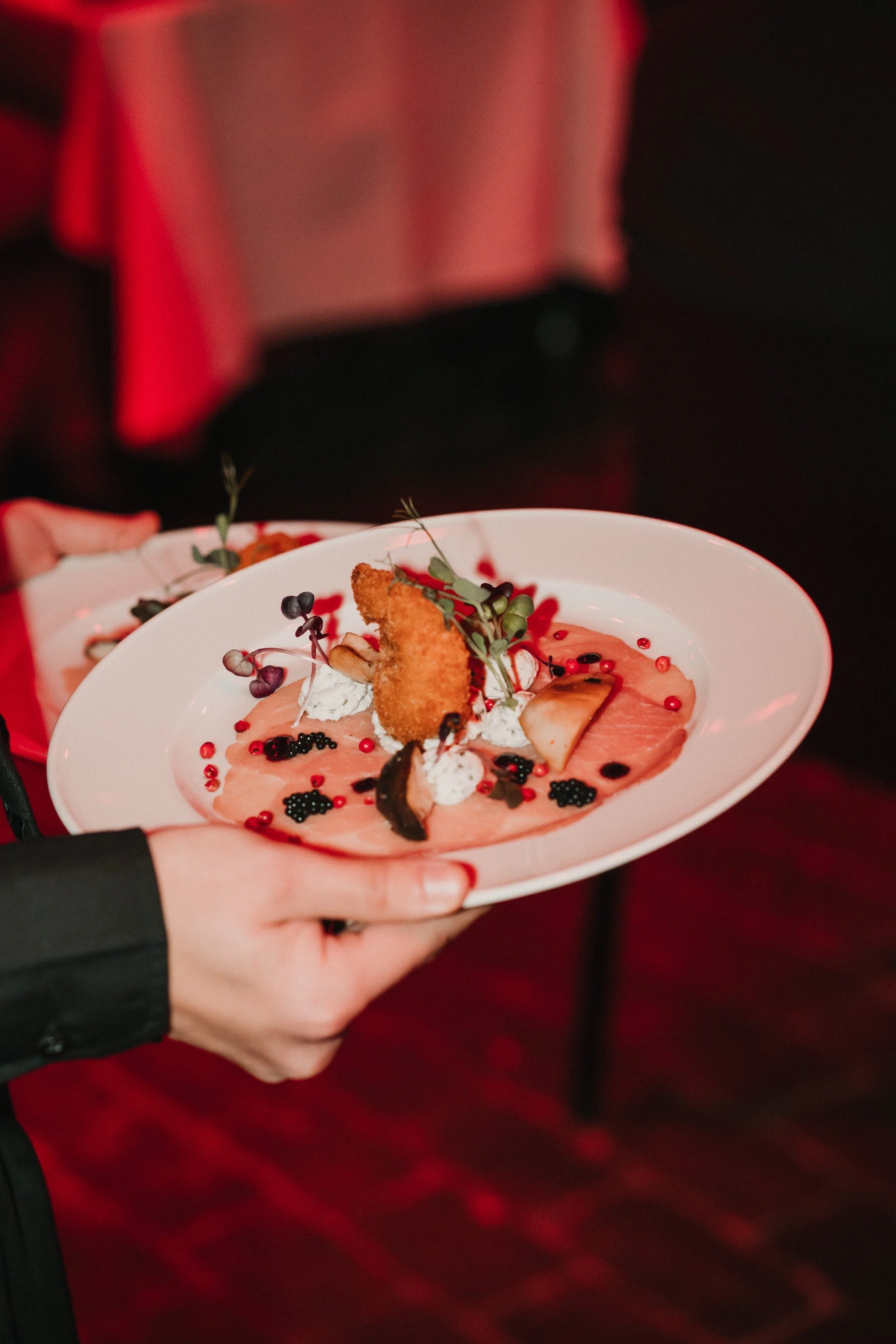 Elegantes Gericht mit geräuchertem Lachs, Garnitur aus Beeren, Kräutern und einer knusprigen Speise auf einem weißen Teller.
