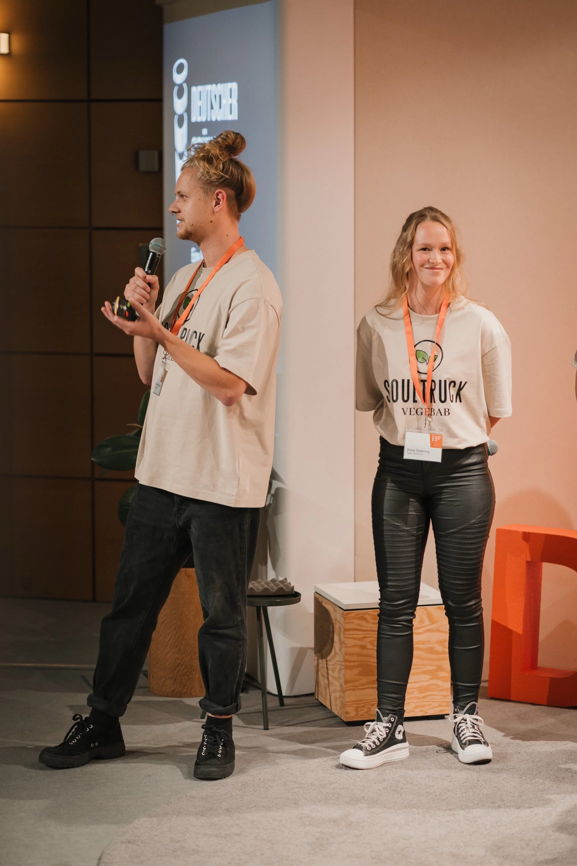 Zwei Personen stehen auf einer Bühne, eine hält ein Mikrofon.