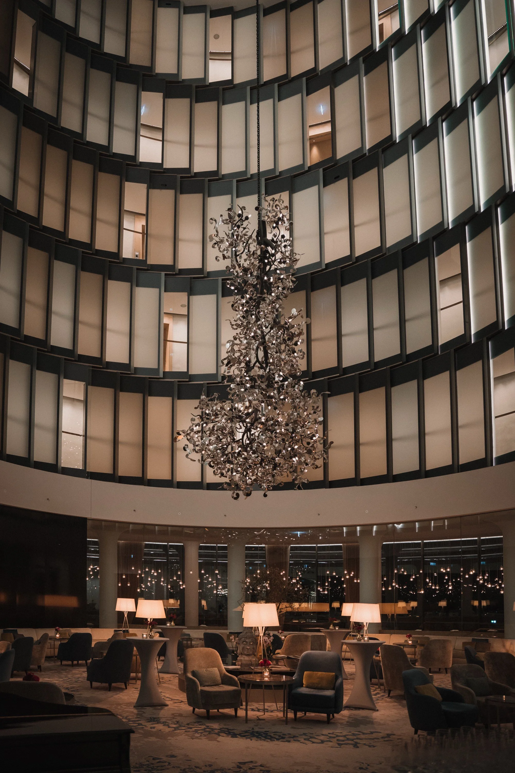 Elegante Hotellobby mit einem großen Kronleuchter, bequemen Sesseln, Stehlampen und glänzenden Fenstern bei Nacht.