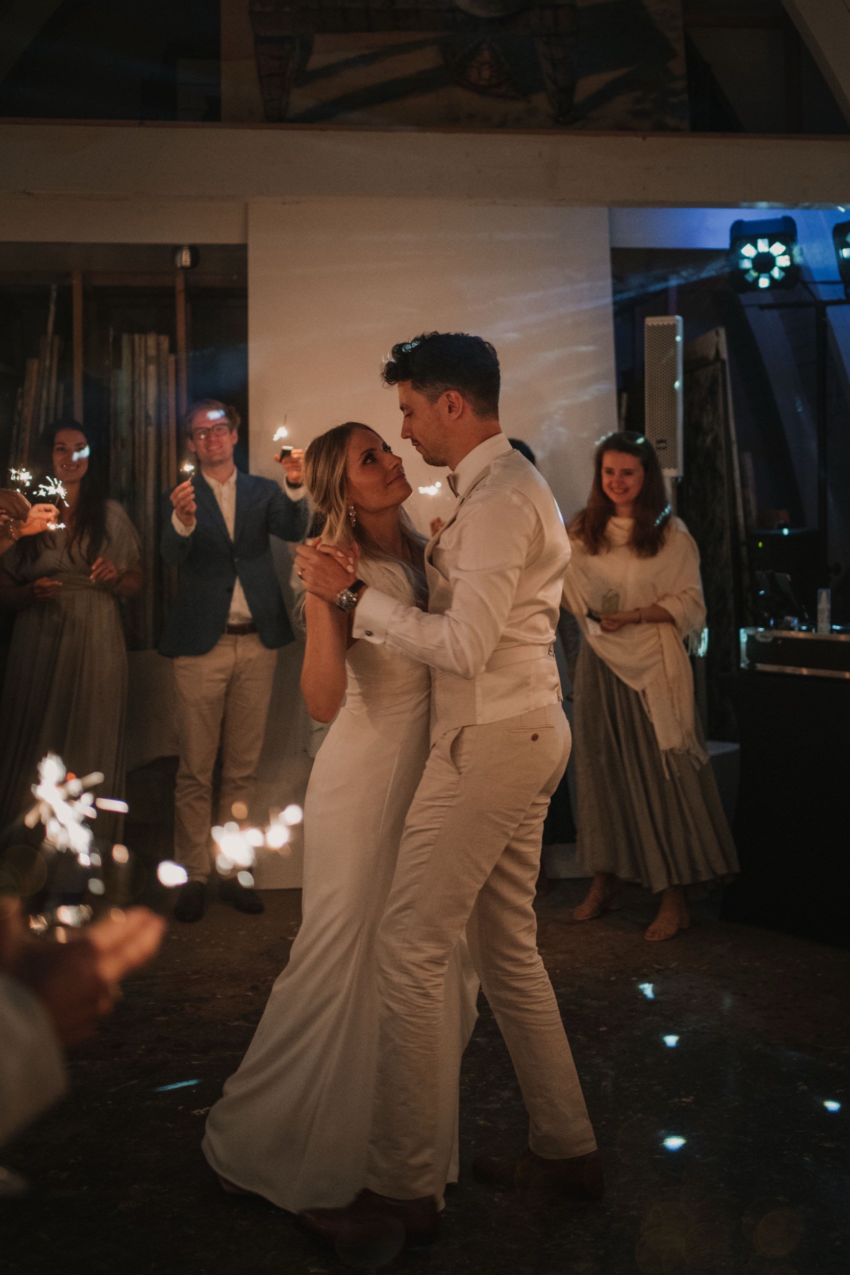 Ein Brautpaar tanzt bei einer Hochzeitsfeier, umgeben von Gästen, die mit Wunderkerzen feiern.