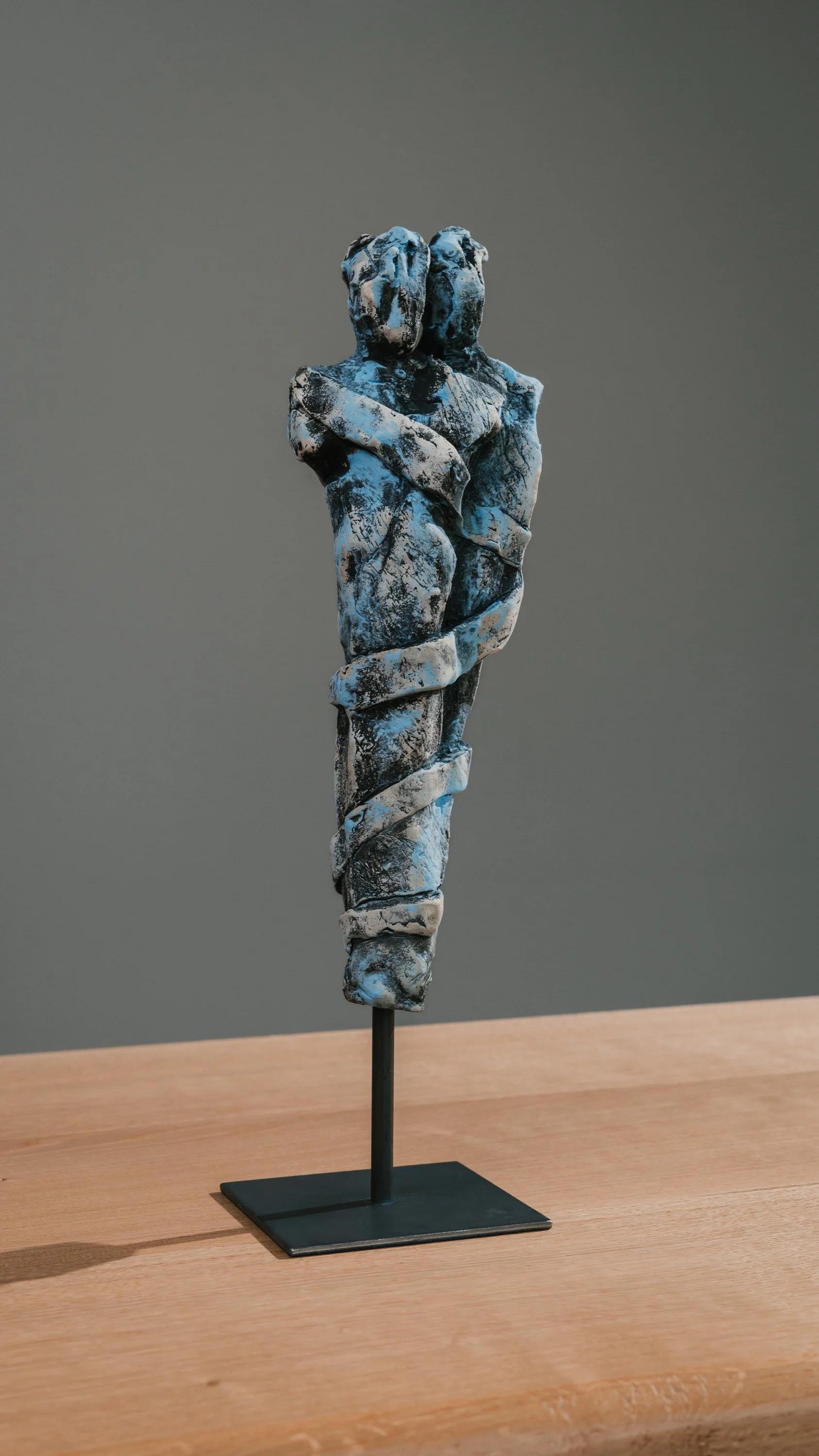 Skulptur eines Paares, das sich umarmt, auf einem schwarzen Ständer, auf einem Holztisch, mit grauem Hintergrund.