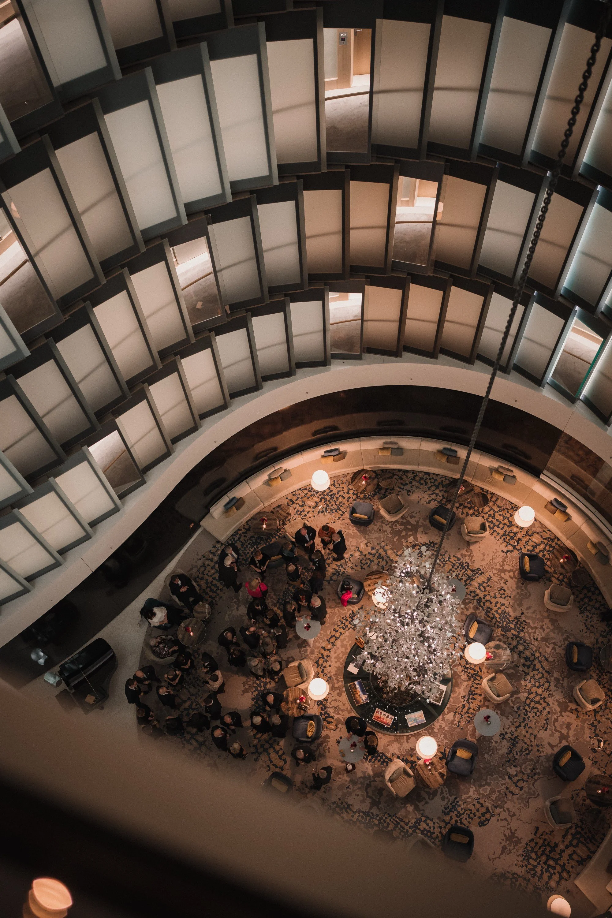 Aufnahme aus der Vogelperspektive eines festlich dekorierten Hotels oder Veranstaltungsortes mit einer großen, baumähnlichen Dekoration in der Mitte, umgeben von mehreren Menschen, Tischen und Sesseln.