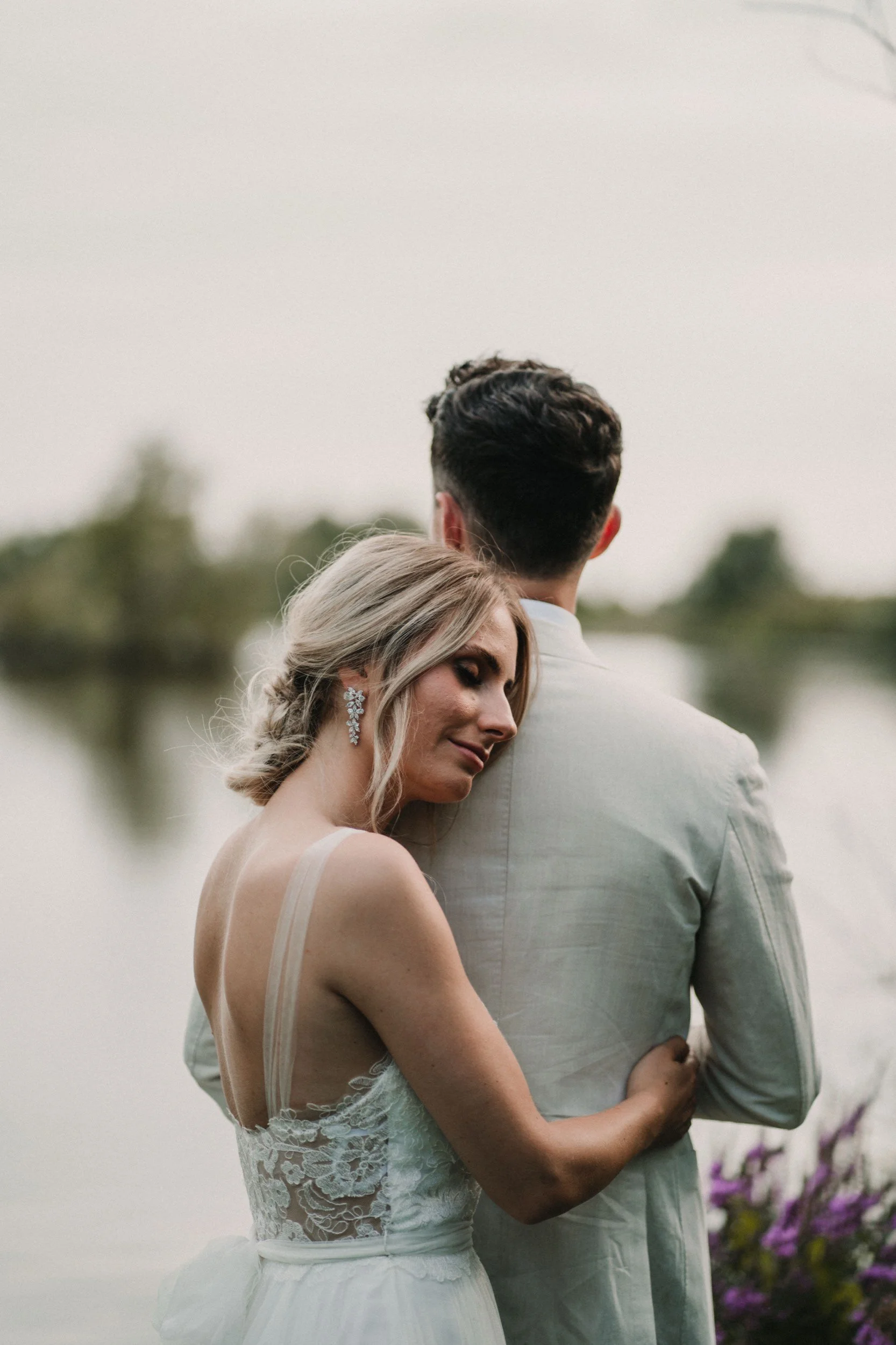 Ein Brautpaar umarmt sich an einem Flussufer bei Sonnenuntergang, mit Rosen im Vordergrund.
