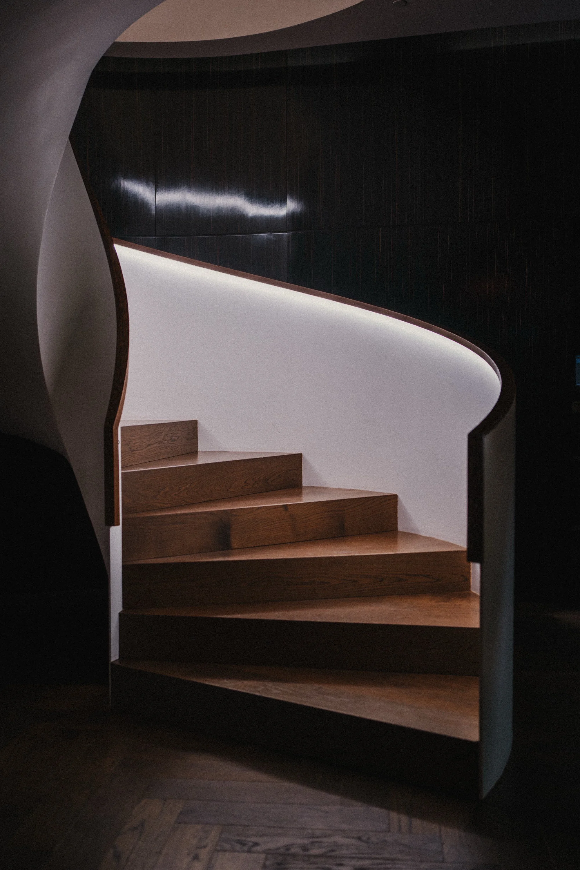 Moderne spiralförmige Holztreppe mit beleuchteter weißer Wand im Hintergrund