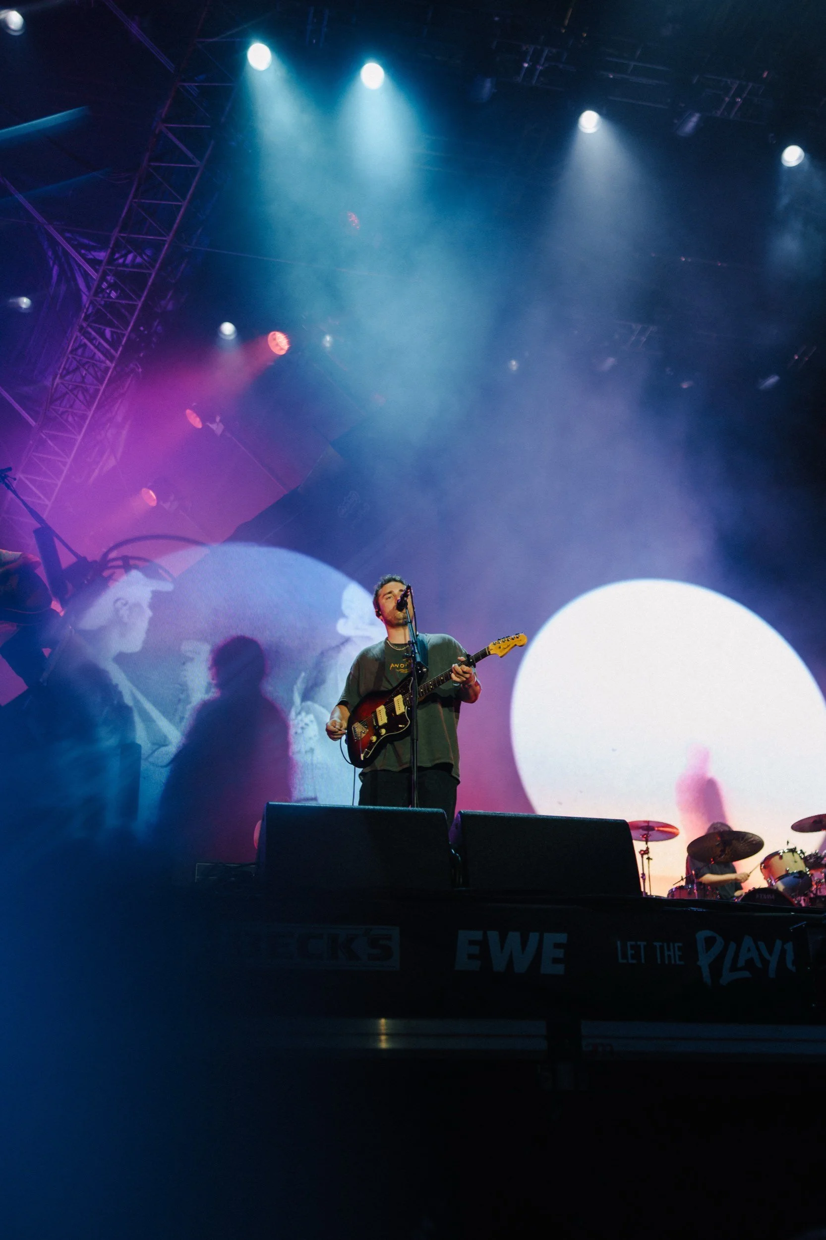 Musiker auf einer Bühne bei einem Konzert, mit leuchtenden Lichtern und einem großen Bildschirm im Hintergrund