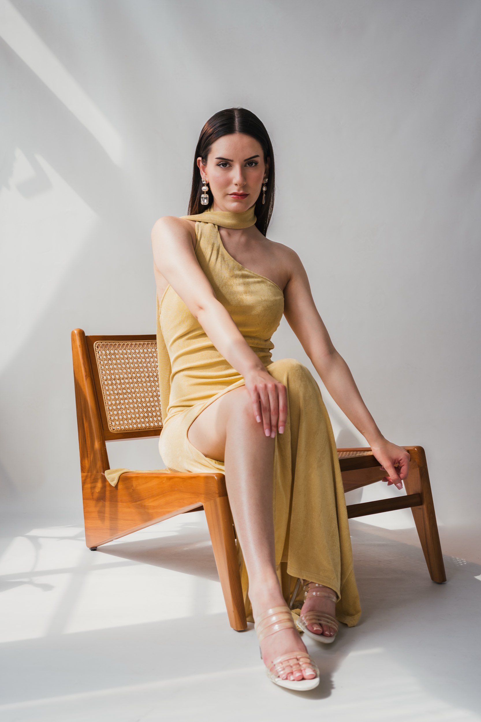 Frau in goldenem Kleid sitzt auf Stuhl in hellem Raum.