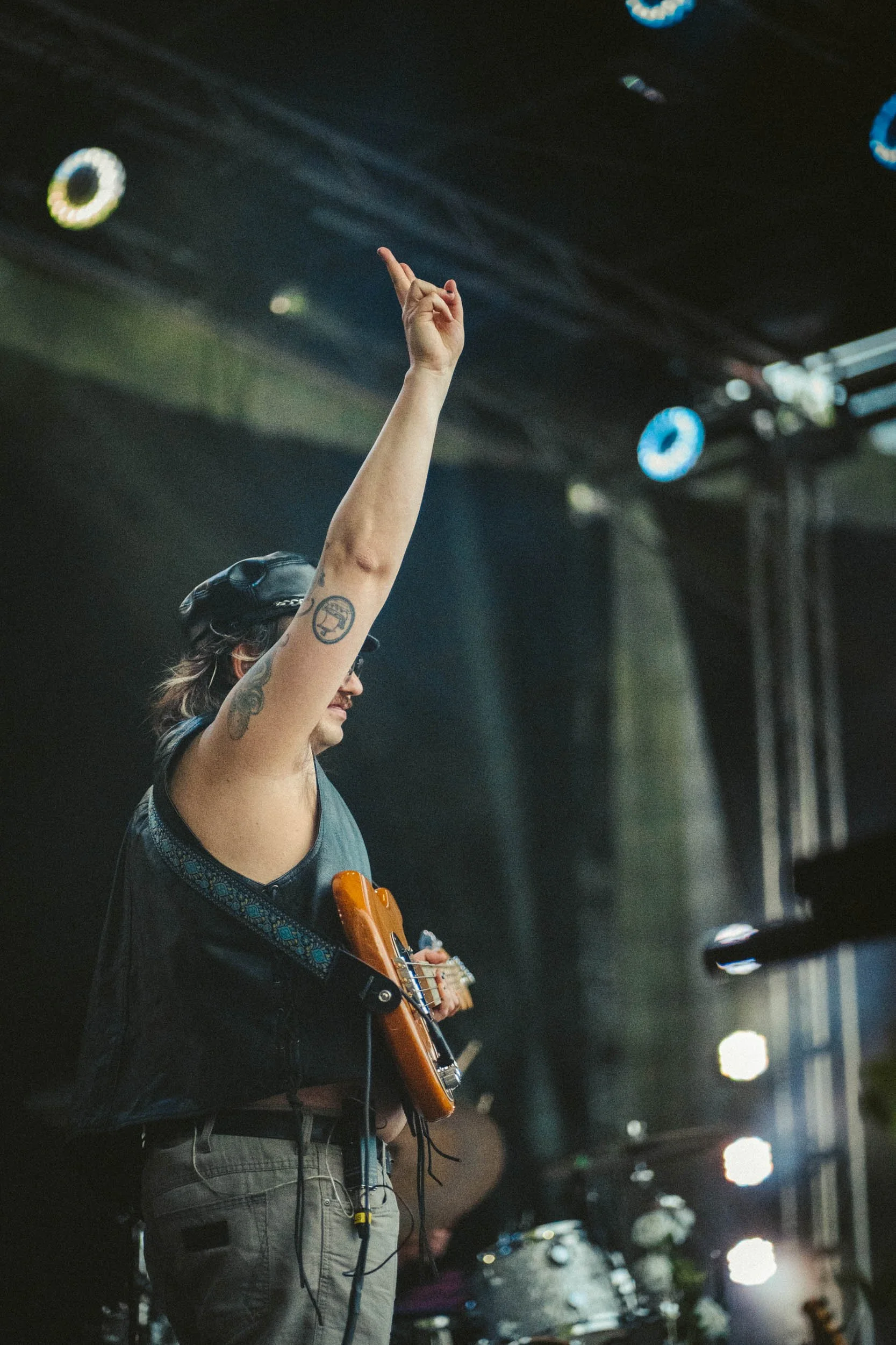 Ein männlicher Musiker auf einer Bühne während eines Auftritts, der eine Gitarre trägt und eine Hand nach oben streckt.