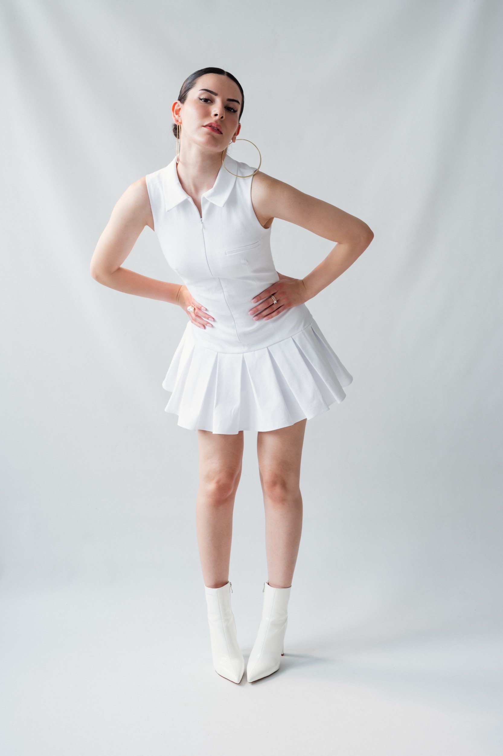 Junge Frau in weißem Kleid und weißen Stiefeln posiert vor einem neutralen Hintergrund.