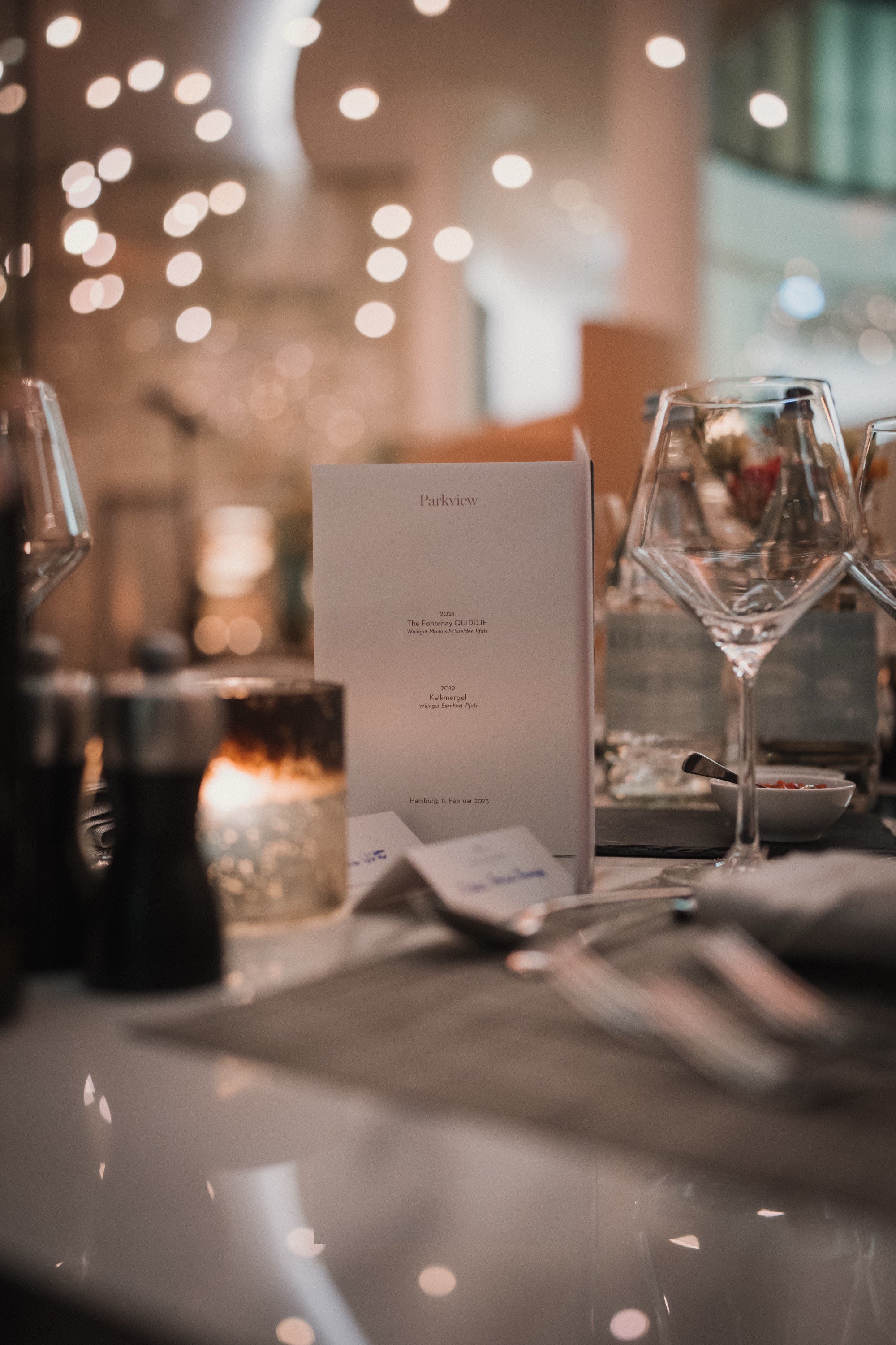 Ein Tisch in einem Restaurant mit Weingläser, Kerze und Menükarten, bei gedämpftem Licht.