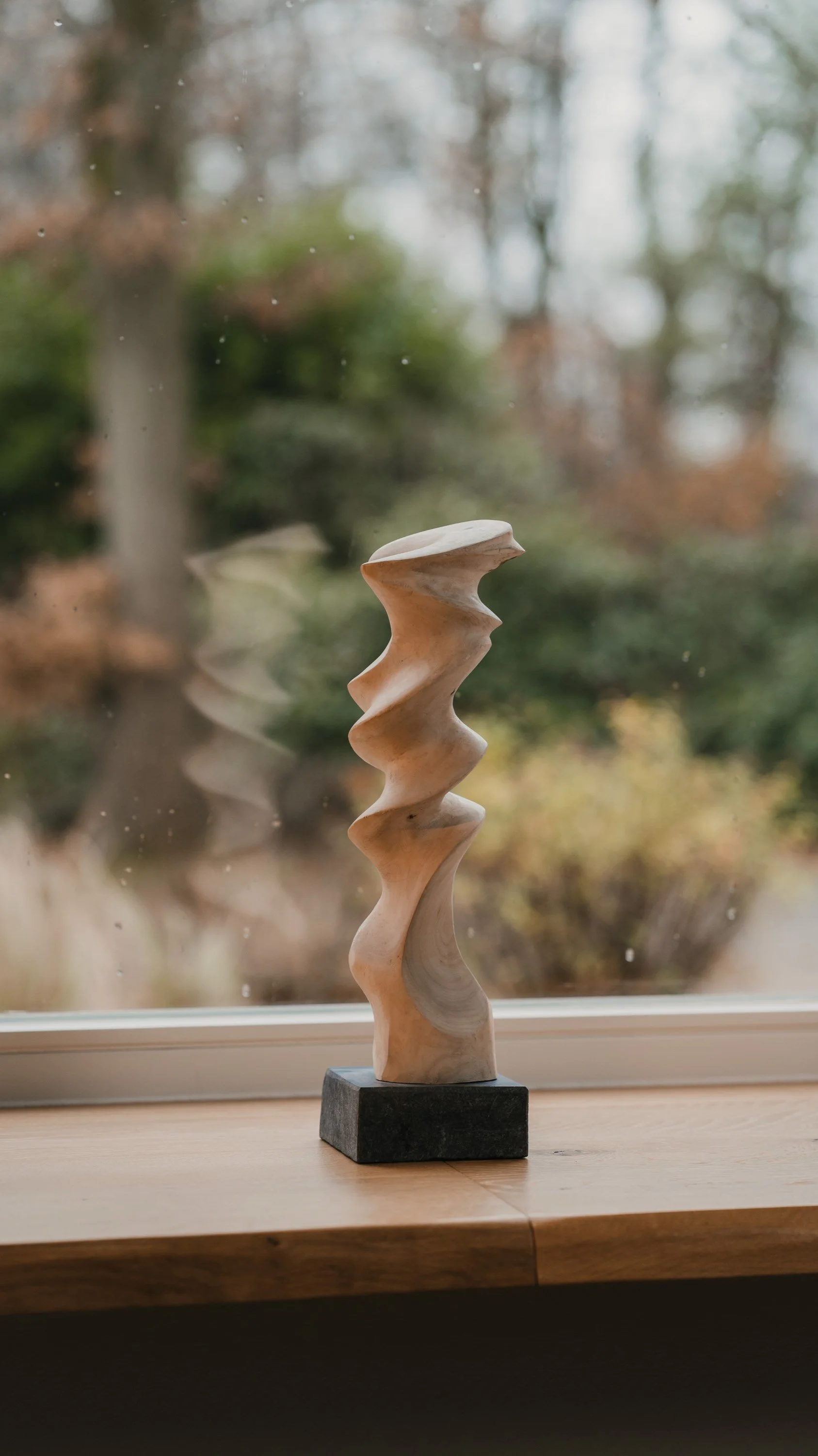 Holzskulptur auf Fensterbank vor einer unruhigen, leicht bewölkten Herbstlandschaft